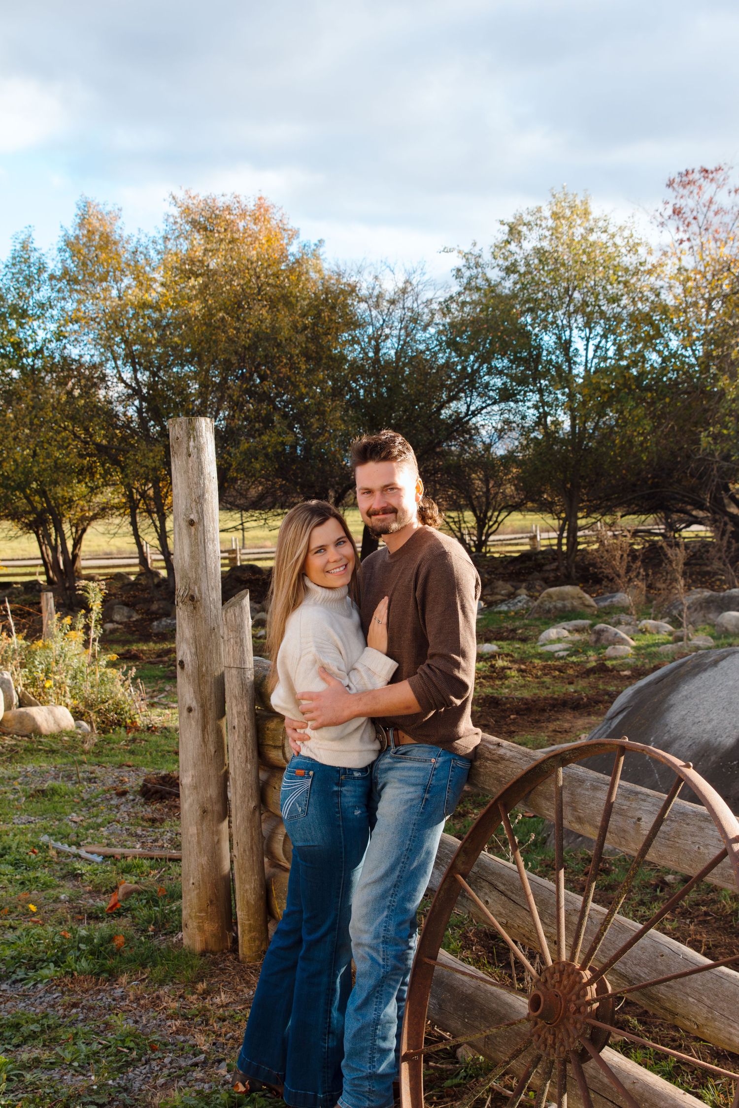 A couple shares an intimate moment by a rustic wooden fence during autumn.