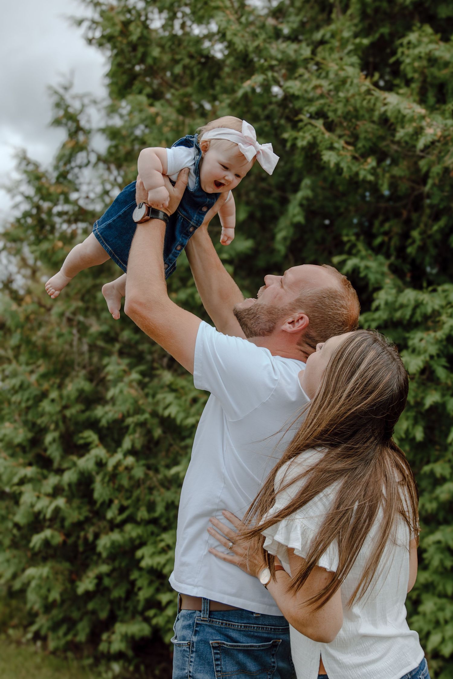 A playful family moment captured outdoors against green foliage.
