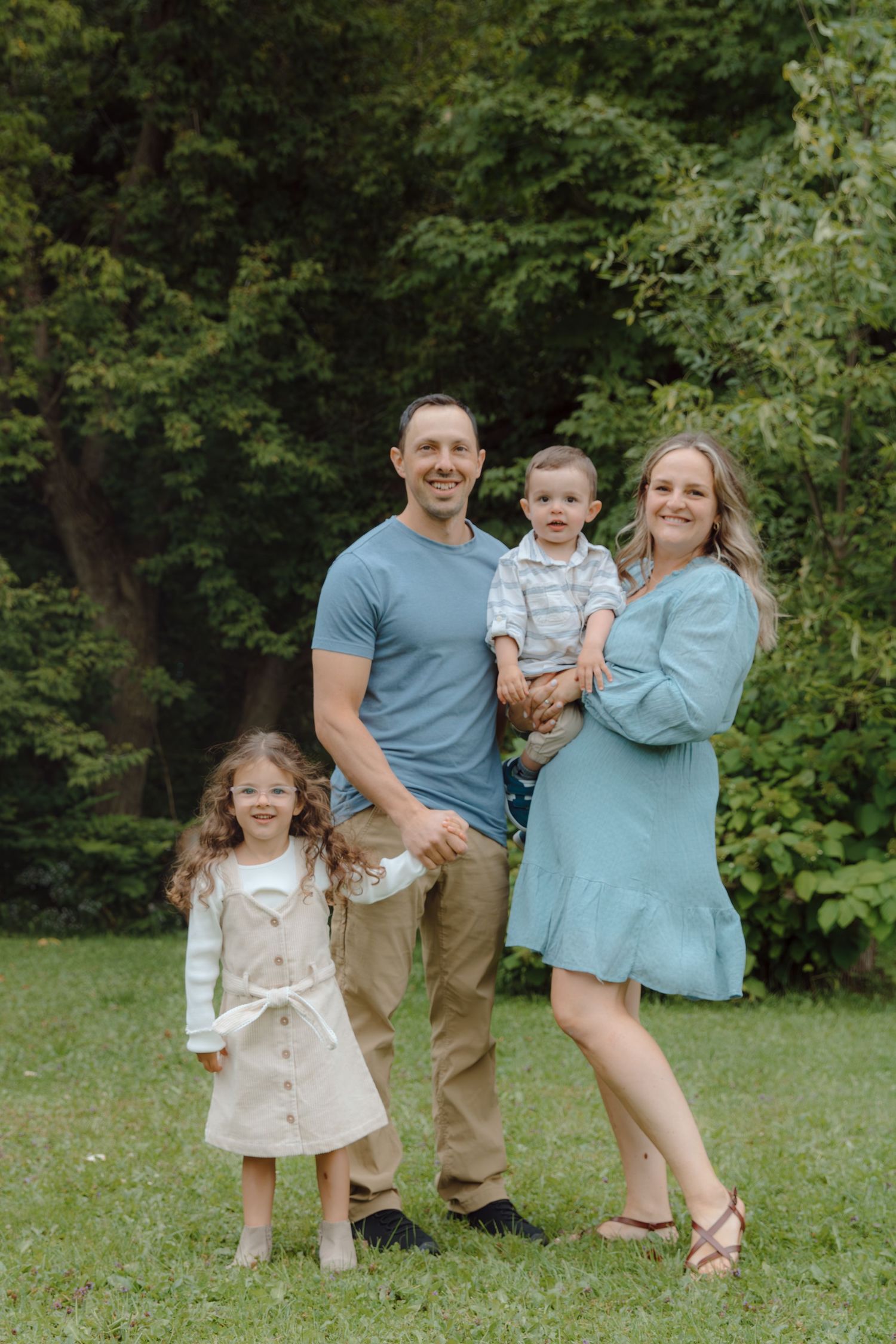 A family portrait taken in a natural outdoor setting with green trees in the background.