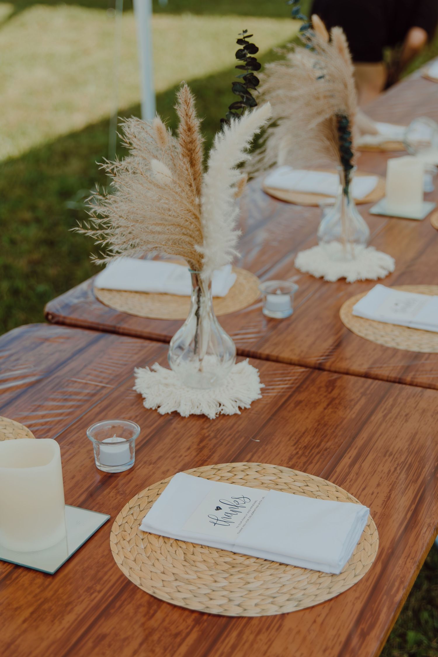 Rustic wooden table setting with pampas grass centerpieces and woven placemats.