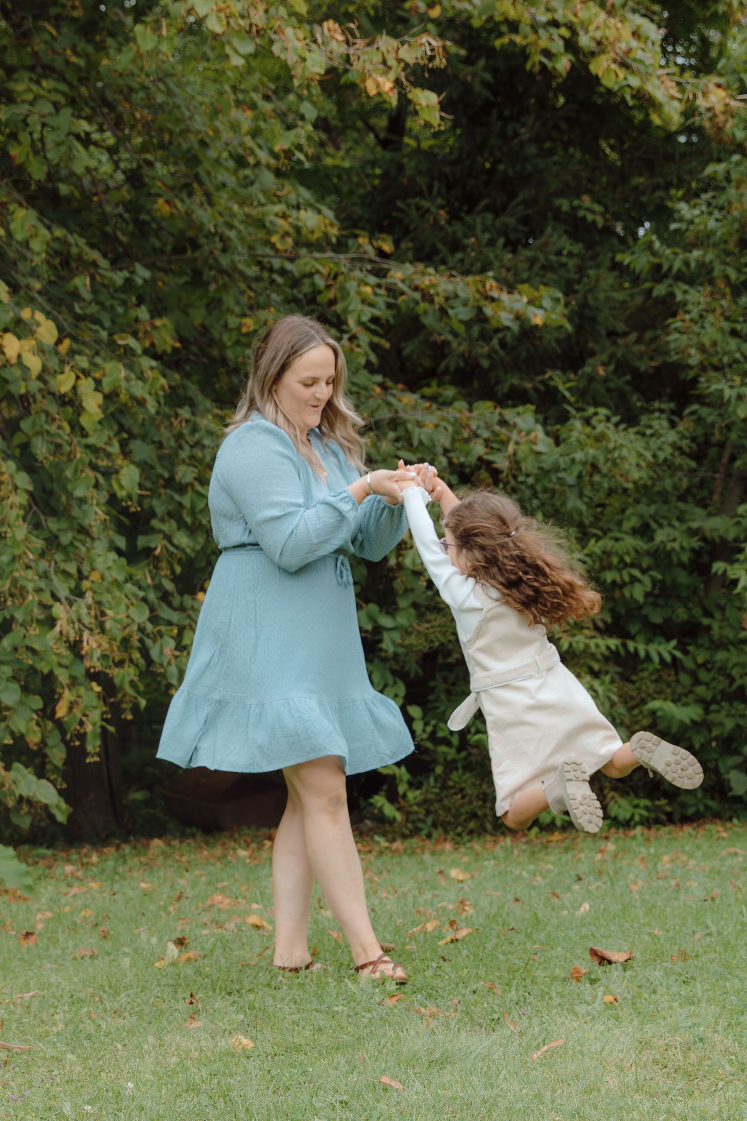 A playful moment captured between parent and child dancing in a green outdoor setting.