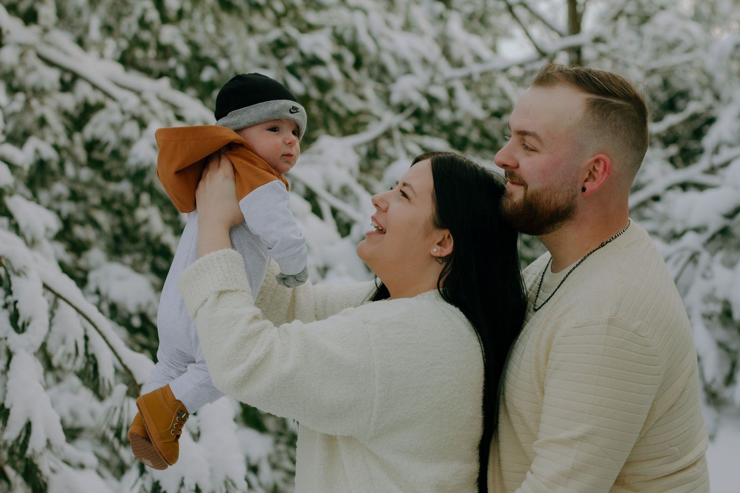 A couple poses together in a snowy winter setting with their dog.