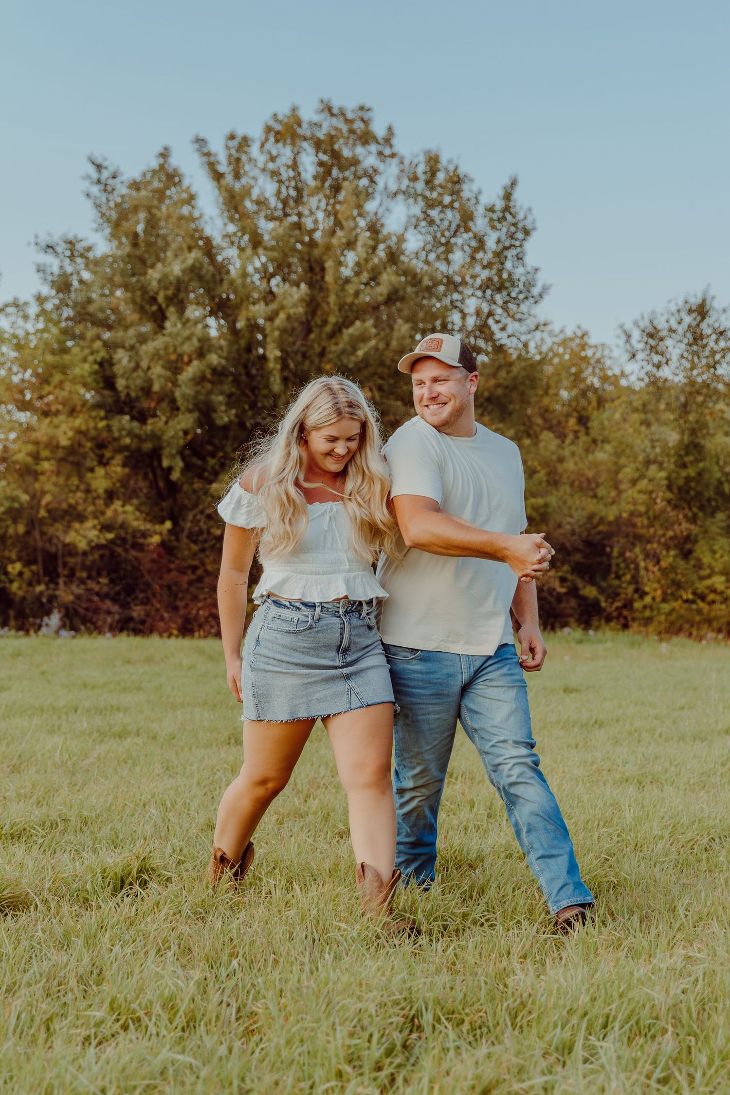 A playful couple walks through a grassy field during a summer photo session.