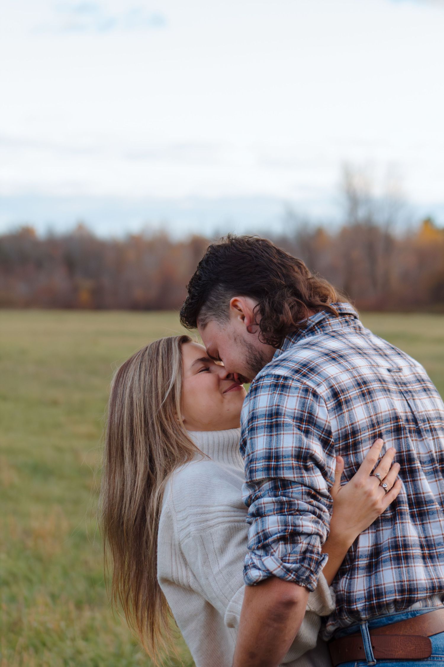 Two people share a romantic embrace in a scenic fall meadow.