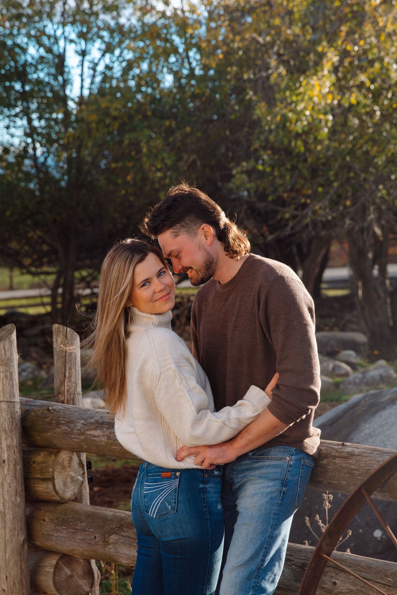 Romantic couple photoshoot by wooden fence during golden hour in autumn setting.