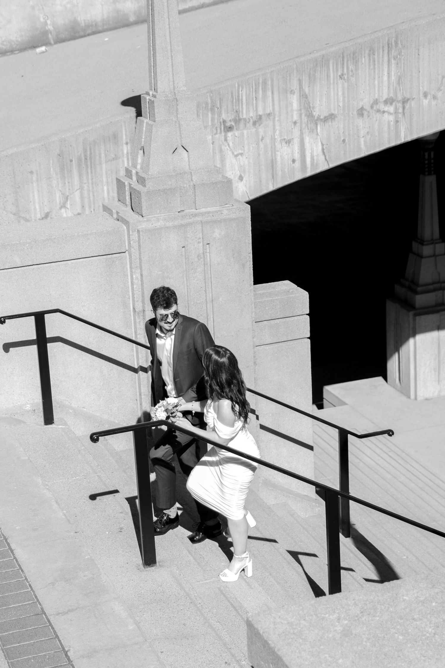 Black and white sequence of two people sitting on stone steps with railings.
