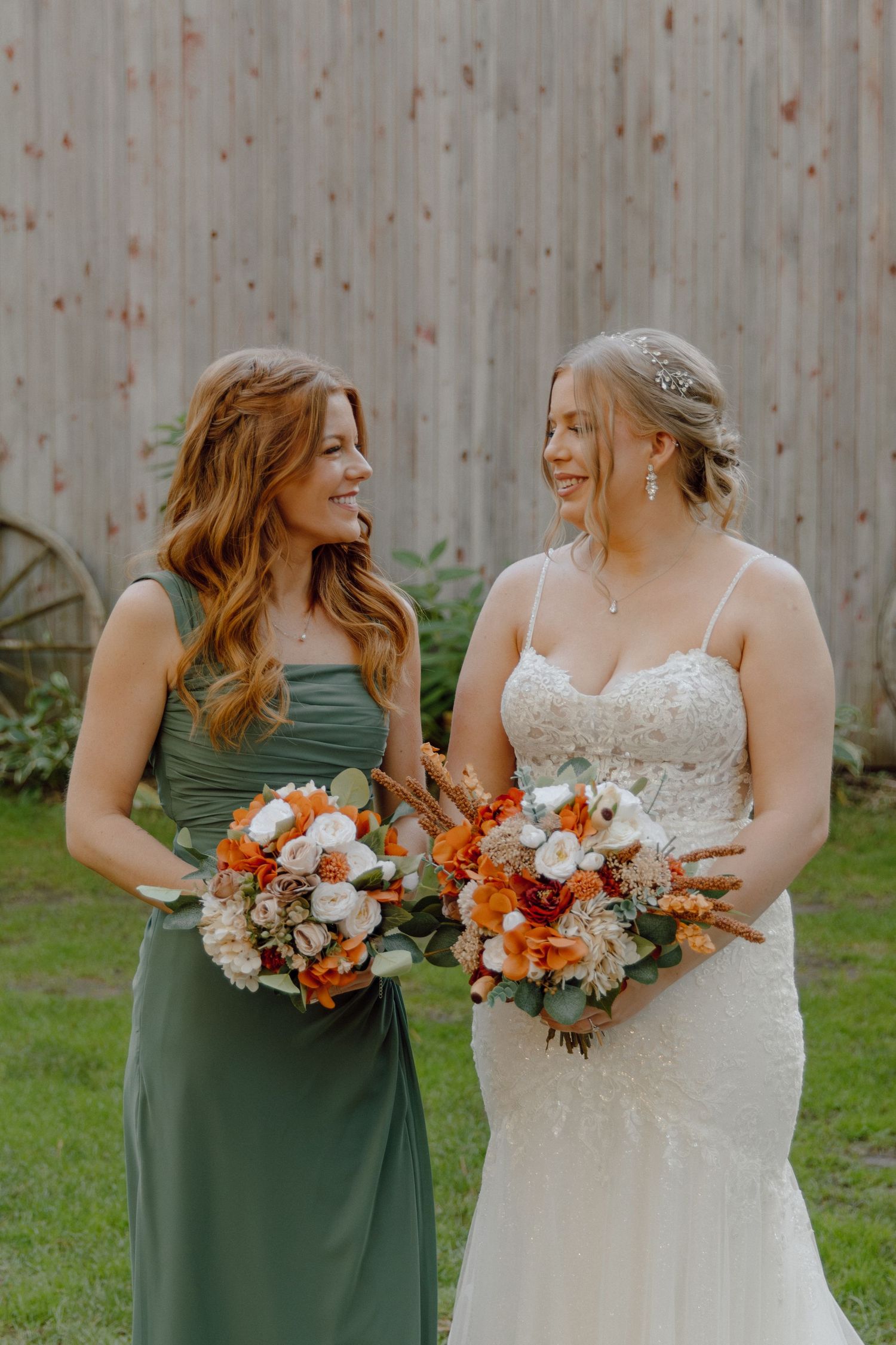 Bride in lace dress and bridesmaid in sage green dress holding autumn-colored bouquets.