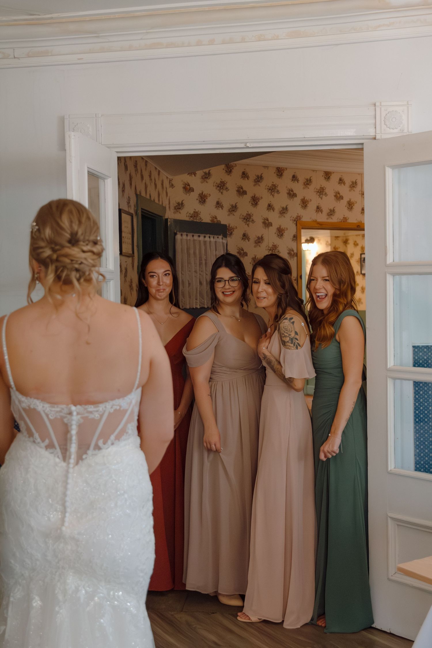 Wedding party in neutral-toned dresses gathered in indoor setting.