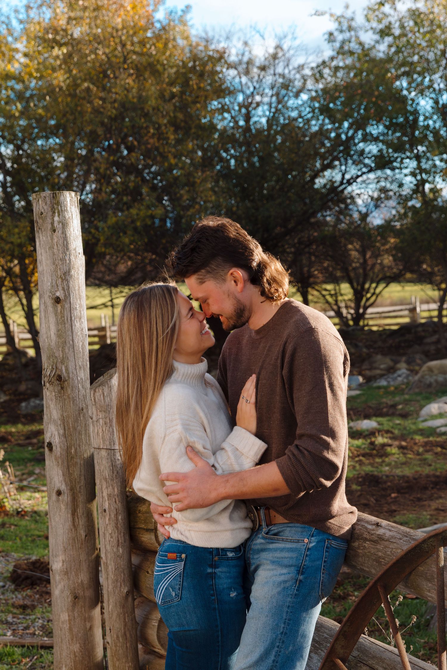 Romantic embrace between a couple near wooden posts and fall foliage.