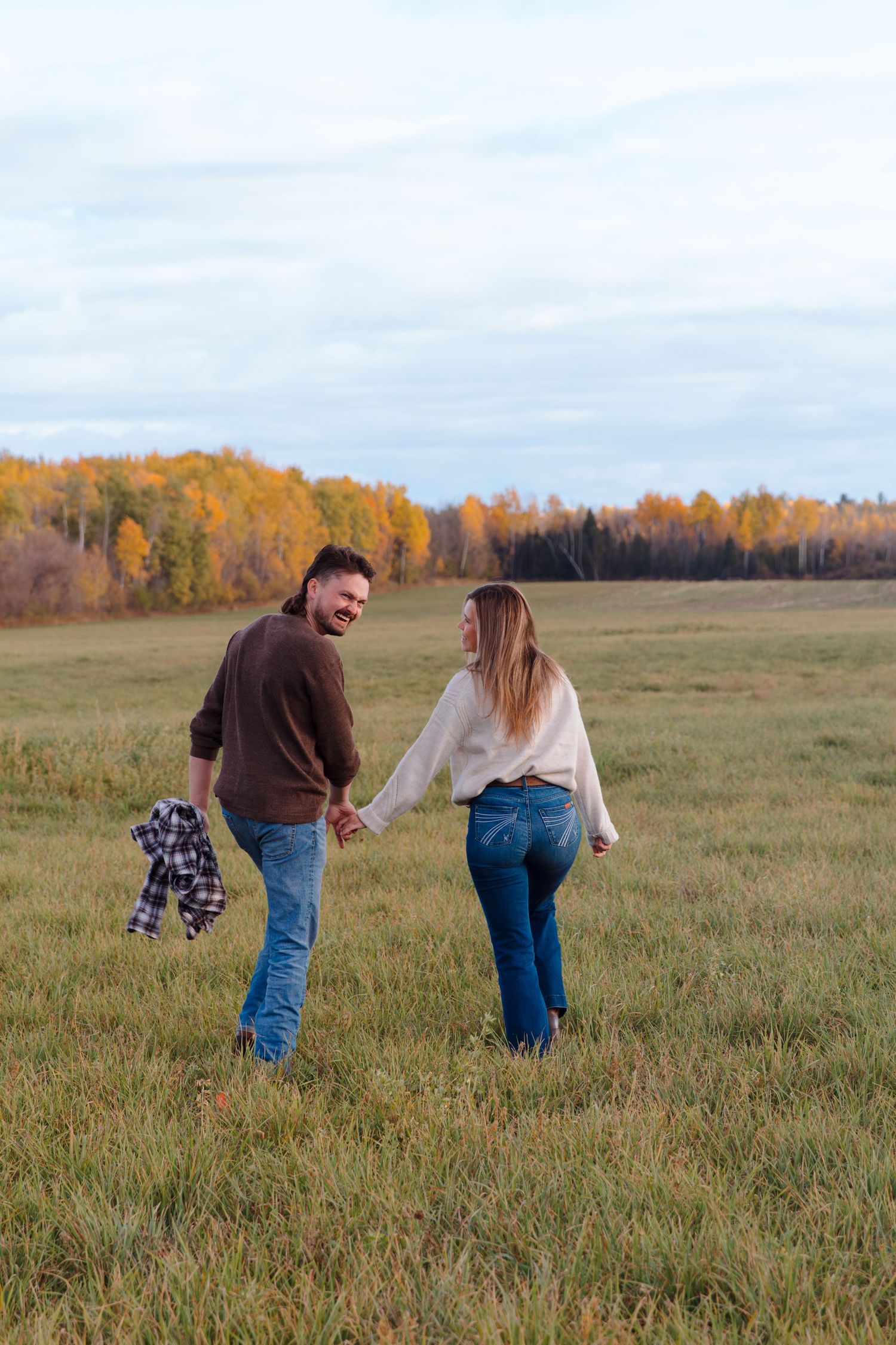 A couple enjoys a playful moment while walking through an autumn field.