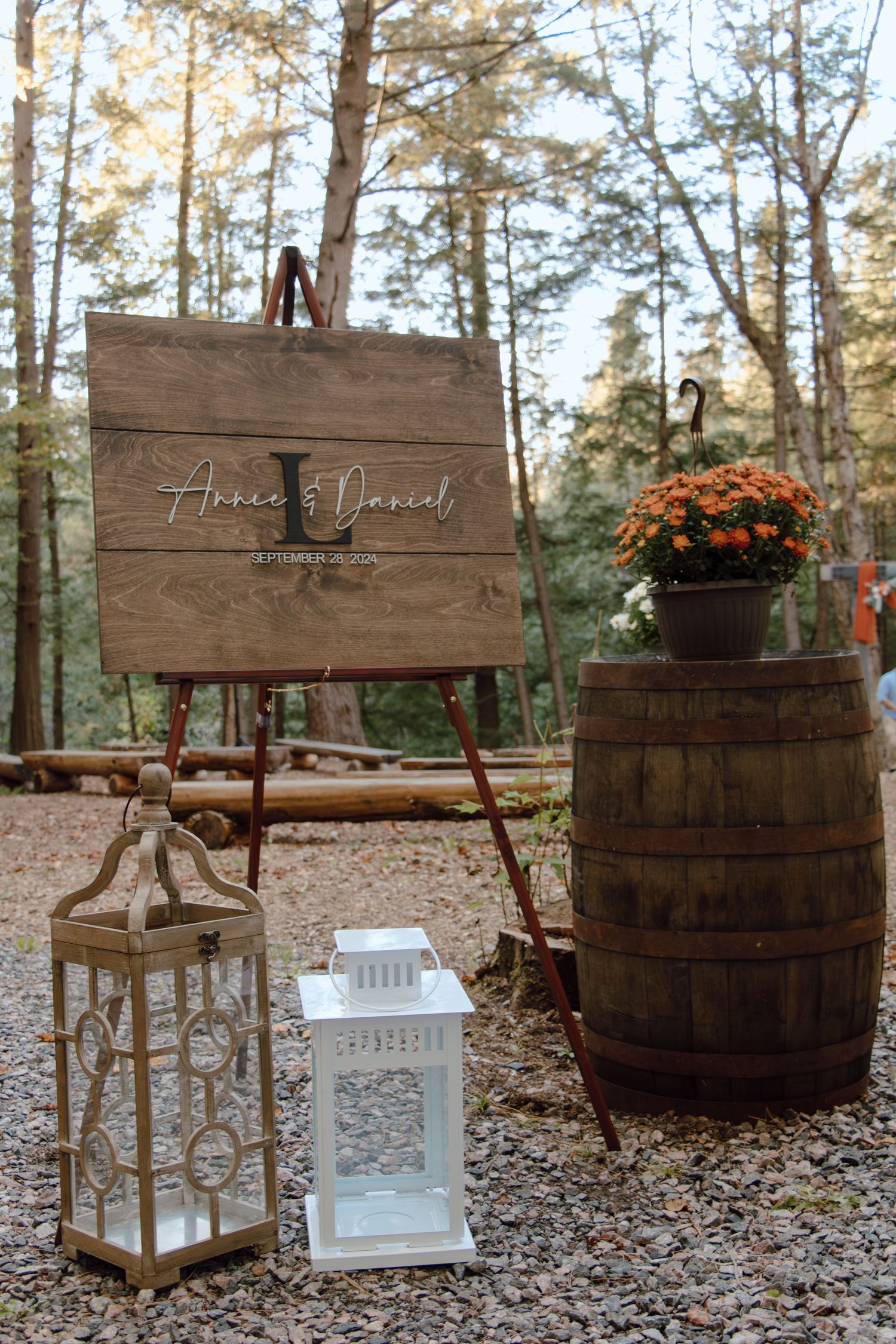 Rustic wedding decor featuring wooden barrels and lanterns arranged outdoors among pine trees.