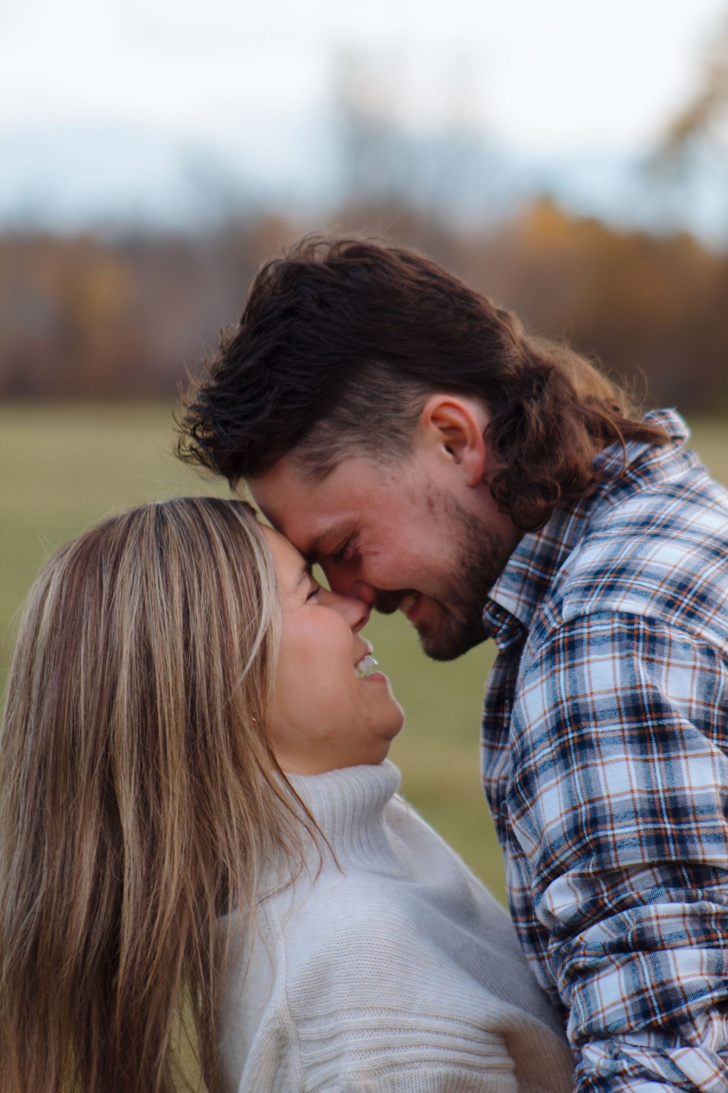A couple leans in close together against an autumn landscape backdrop.