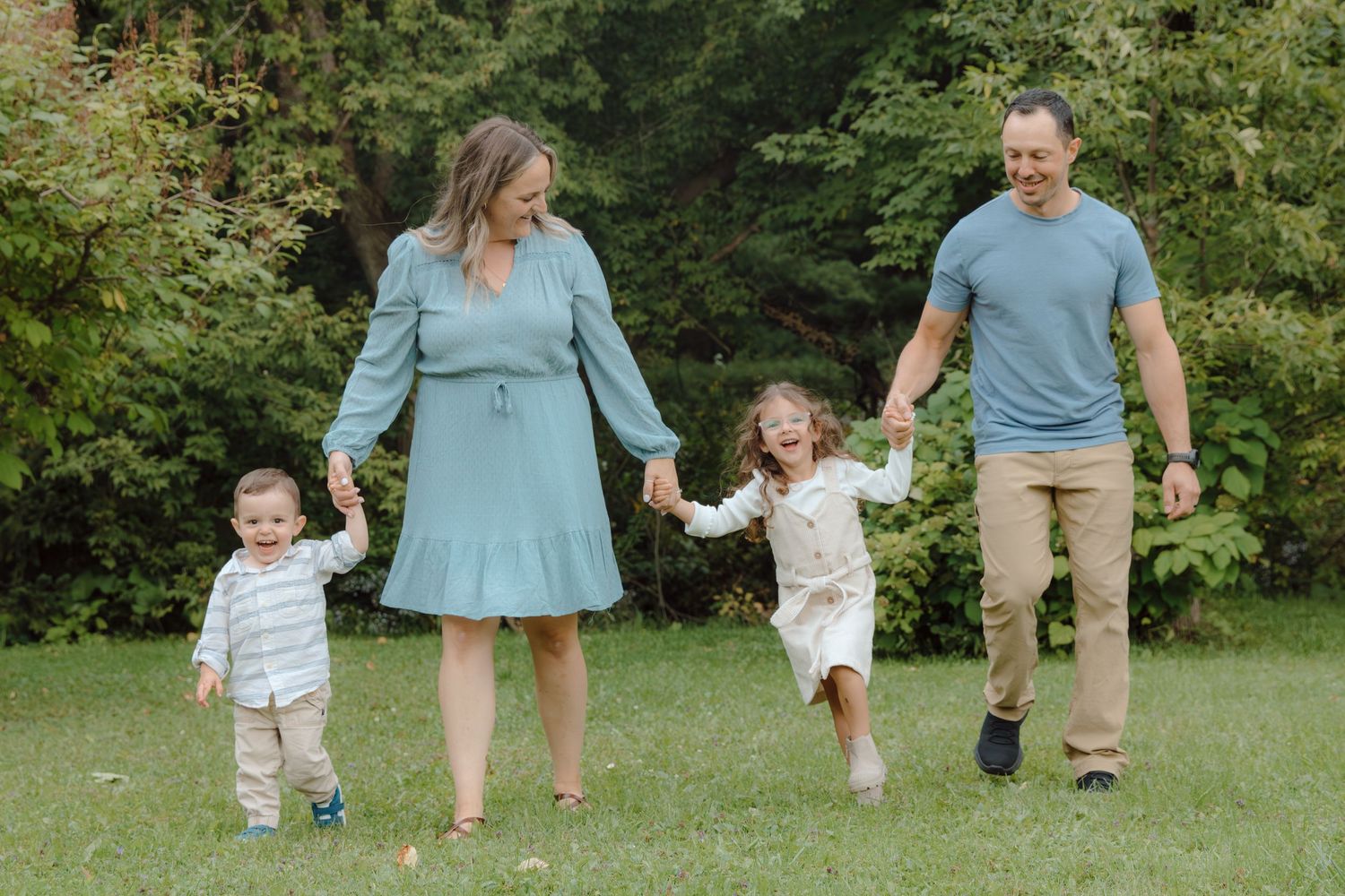Family walking together on grass with trees in the background during a fall day.