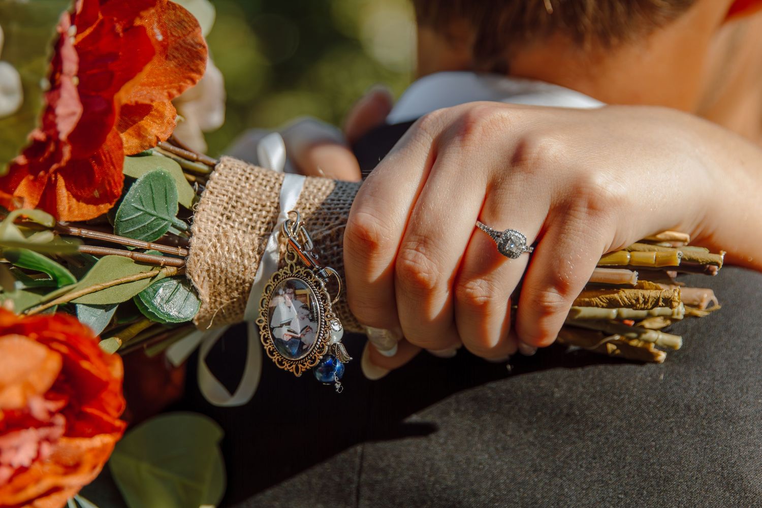 Wedding rings displayed with red flowers and burlap wrapped bouquet in natural lighting.
