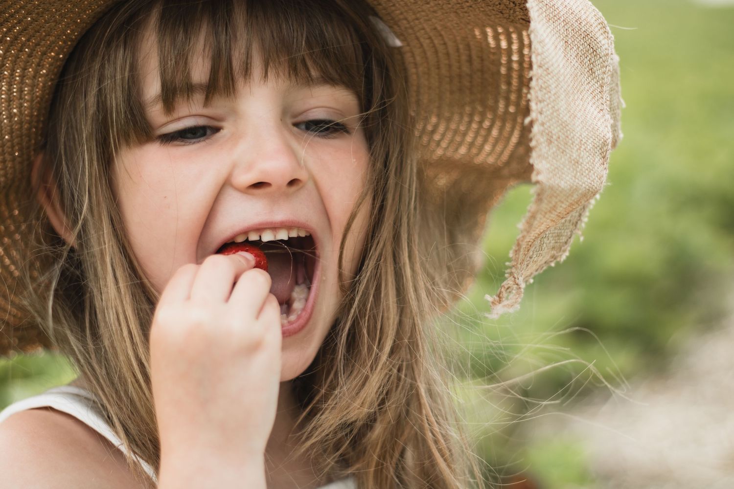 Child wearing straw hat laughing joyfully in natural outdoor setting.