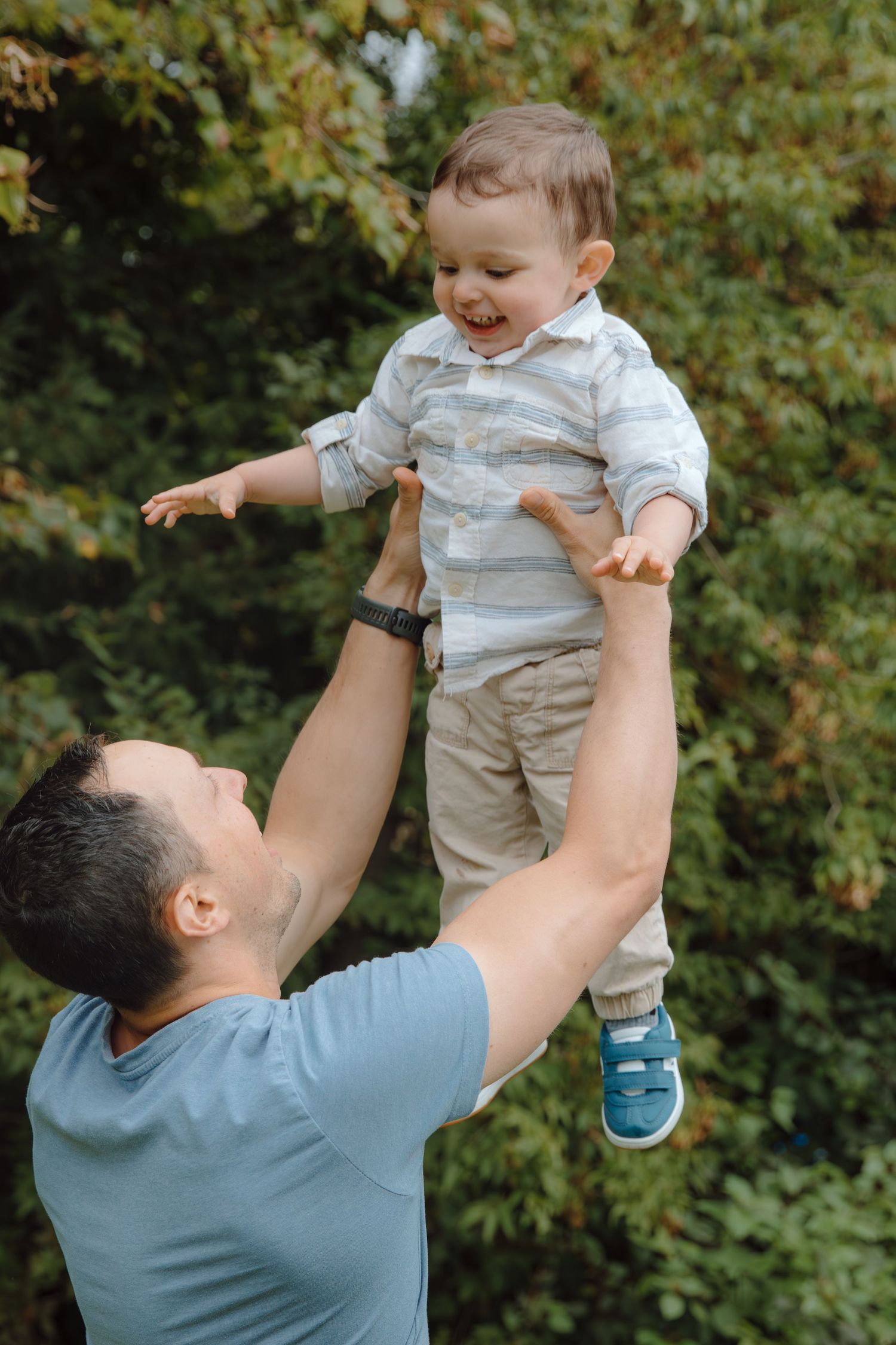 A parent lifts and plays with a toddler wearing a white shirt and khaki shorts in a series of outdoor photos.