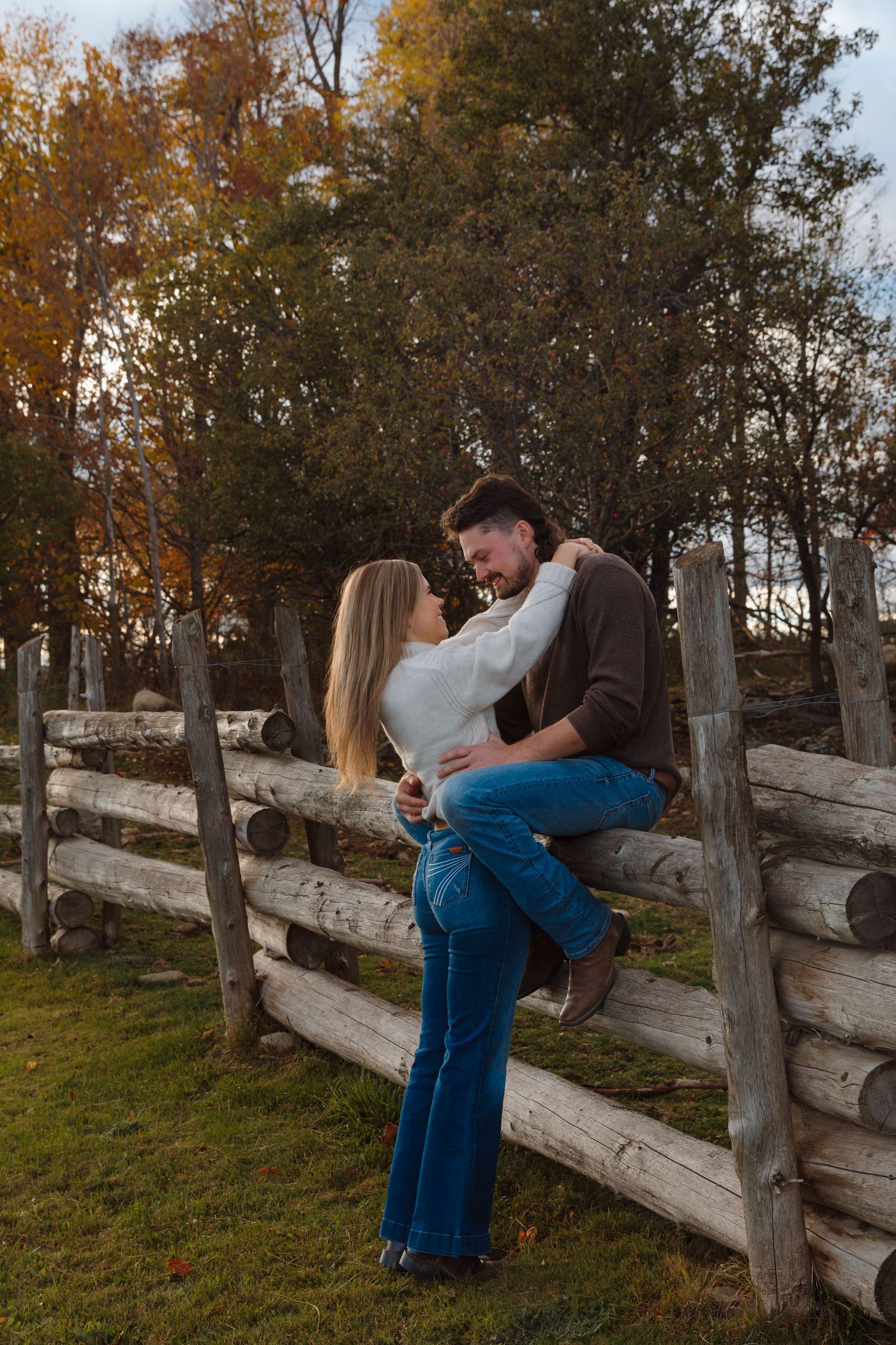 A romantic autumn scene with two people sitting on a wooden fence at sunset.
