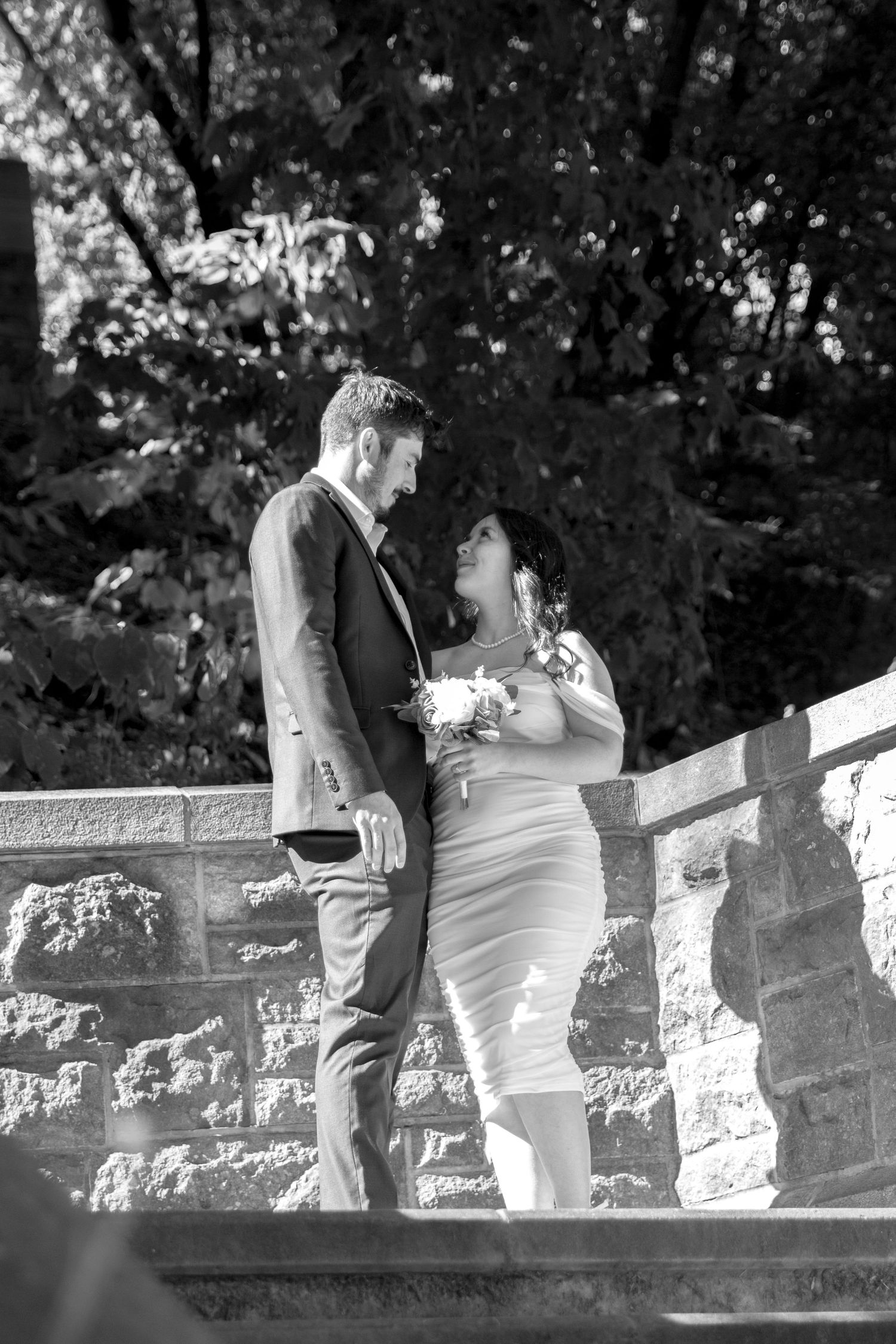 Black and white sequence of two people posing by a stone wall in a garden setting.