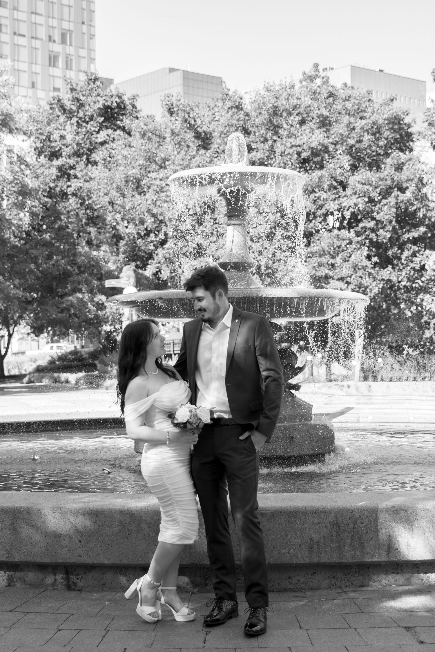 Romantic couple dancing near fountain in urban park setting.