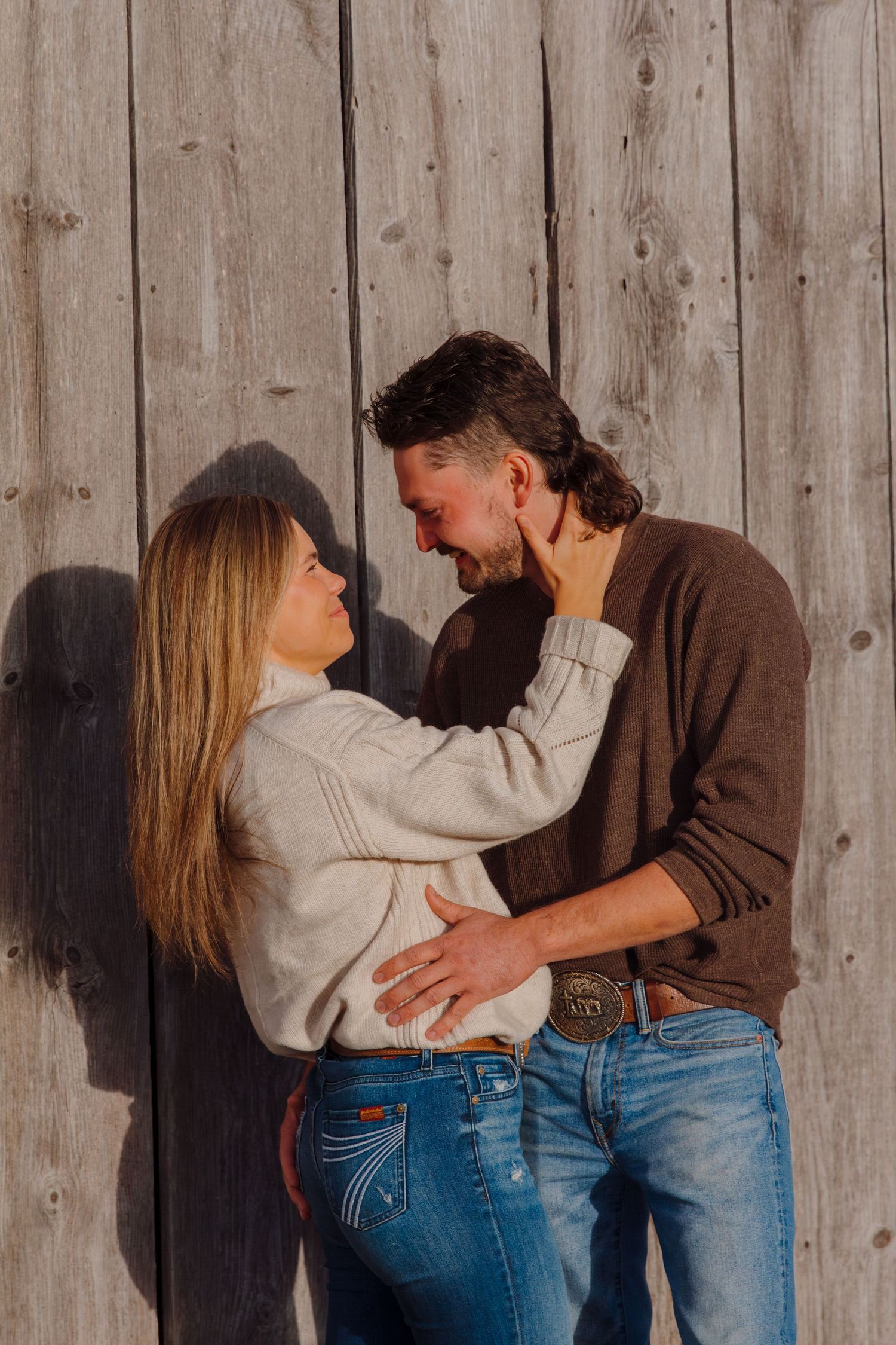 Couple sharing intimate moment against wooden barn wall in natural light.