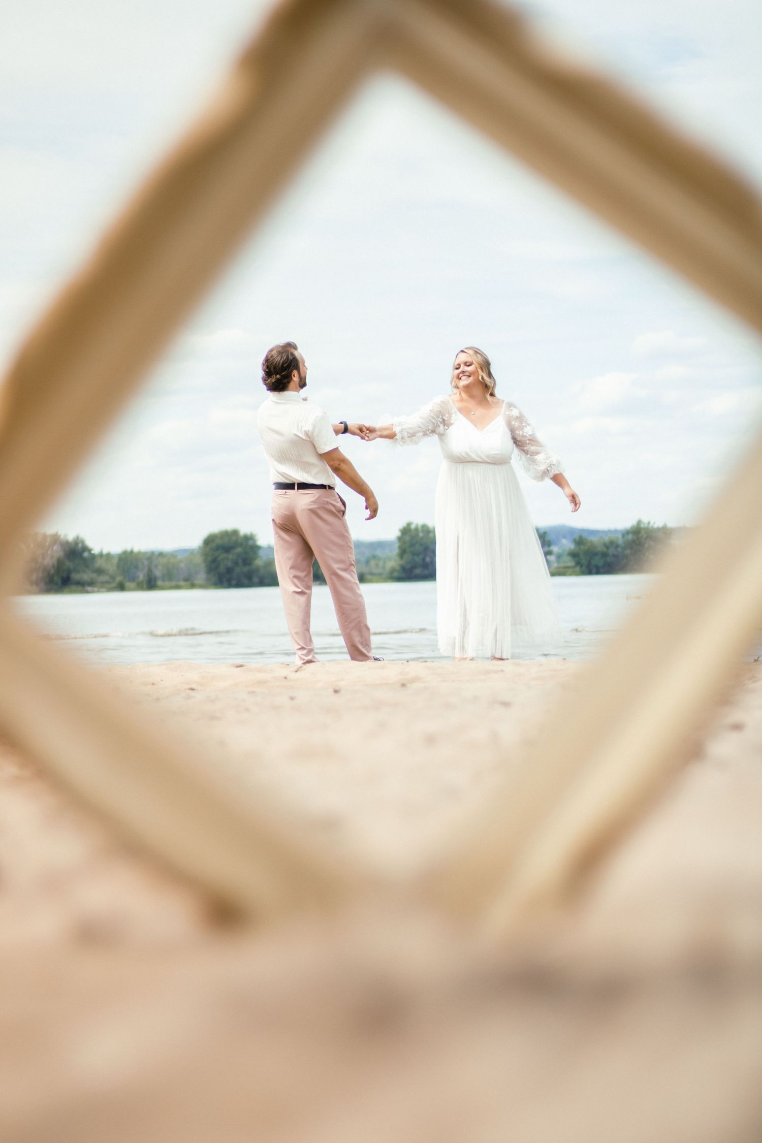 Two figures in white outfits dance together on a sandy beach.
