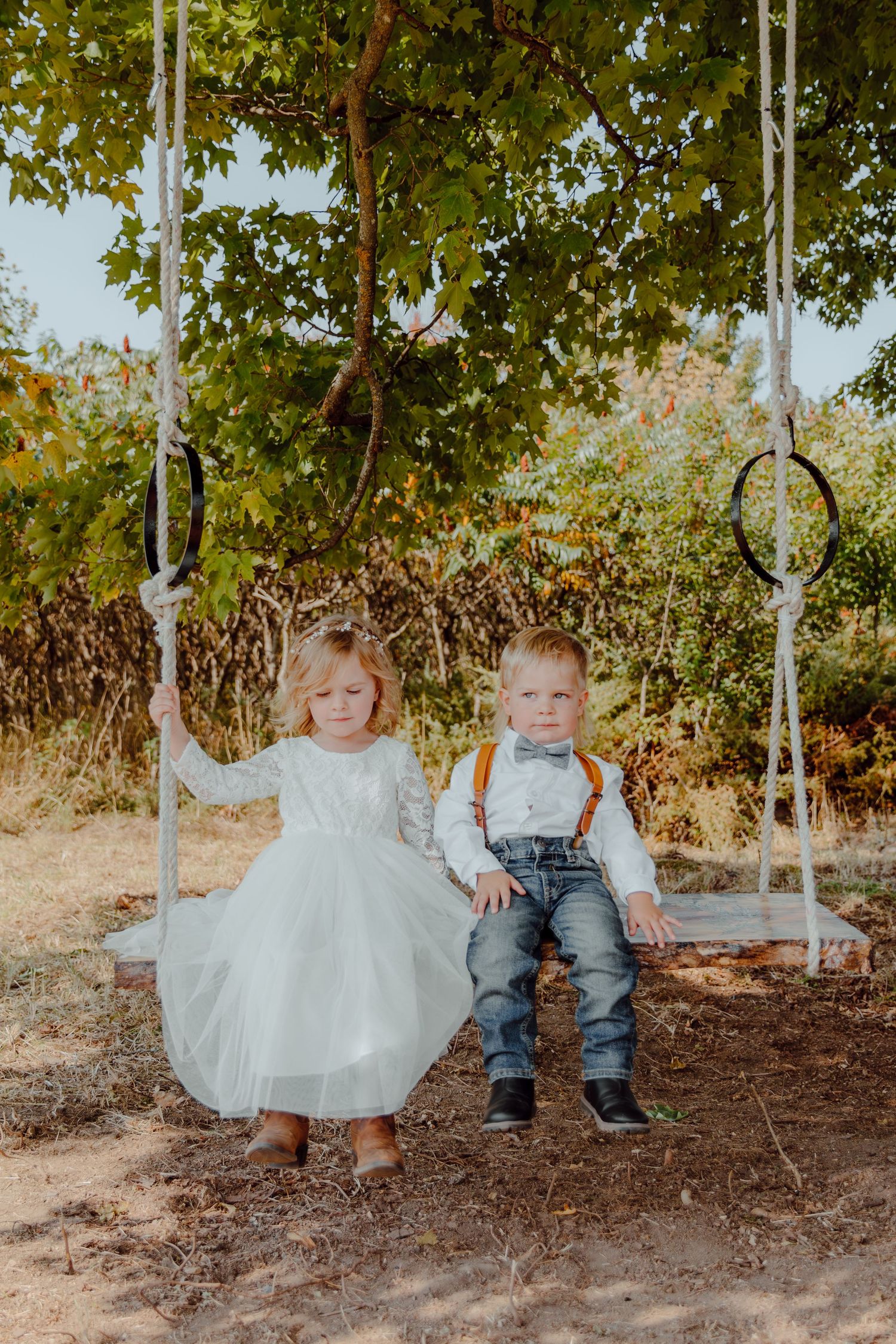 Children playing on a wooden swing set outdoors, dressed in white and denim.
