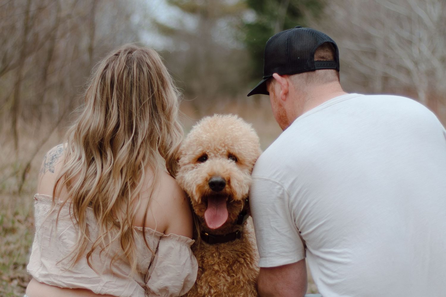 A couple and their goldendoodle dog share loving moments in an outdoor photoshoot.
