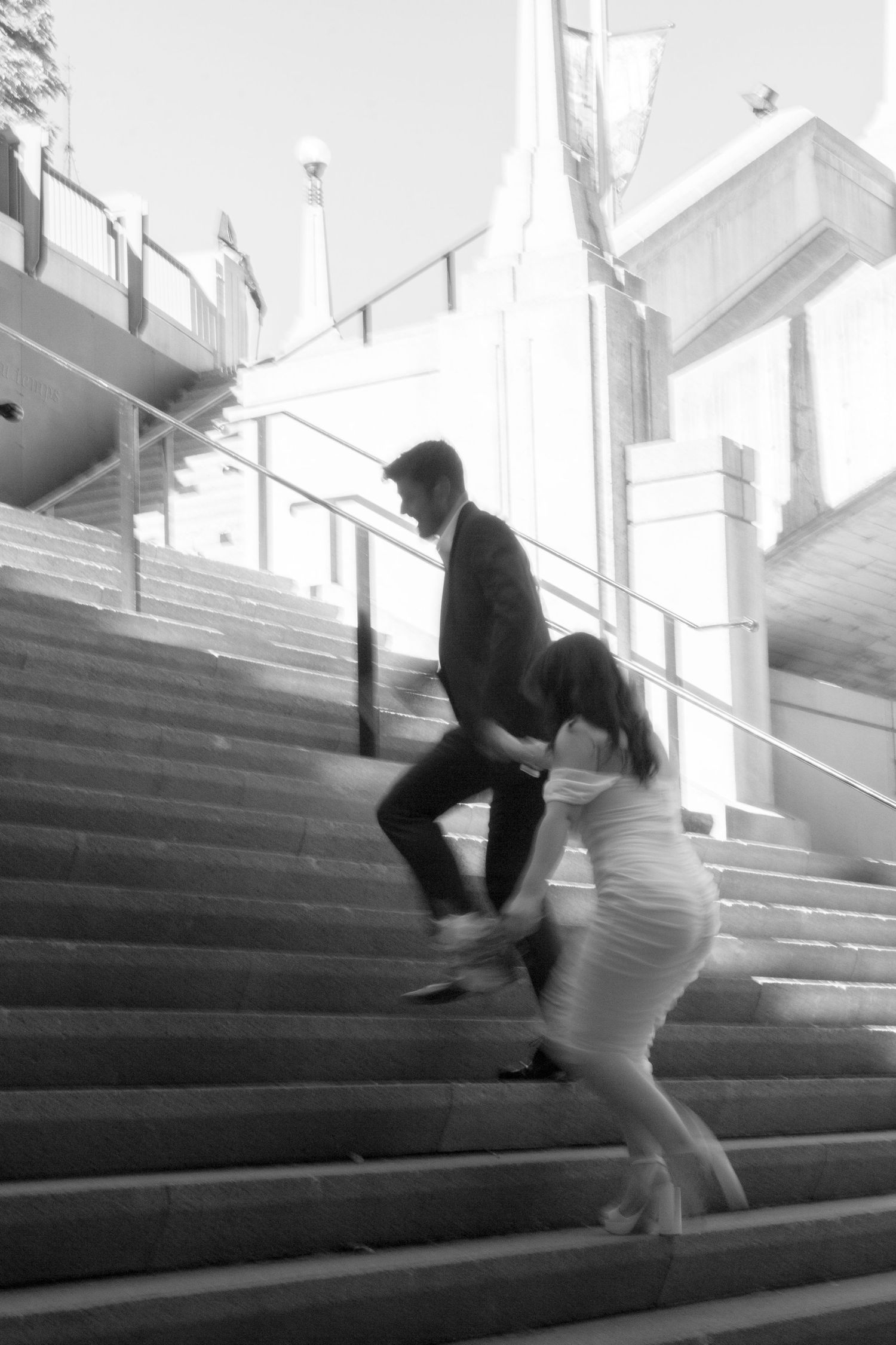 Wedding couple descends concrete stadium steps in playful poses.