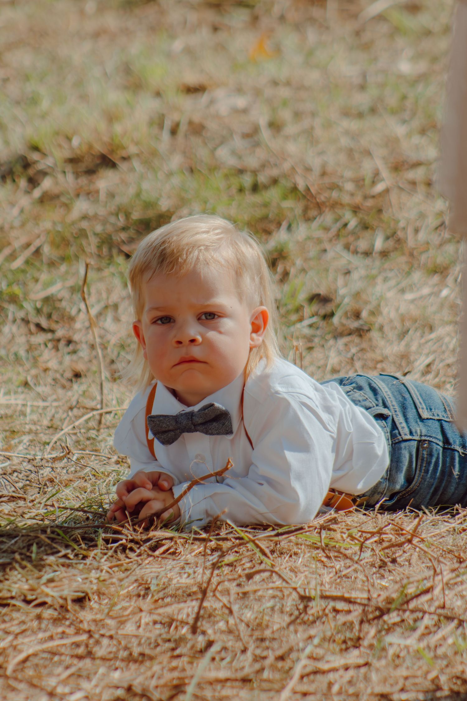 A small child in formal wear lying on autumn leaves looking at the camera.