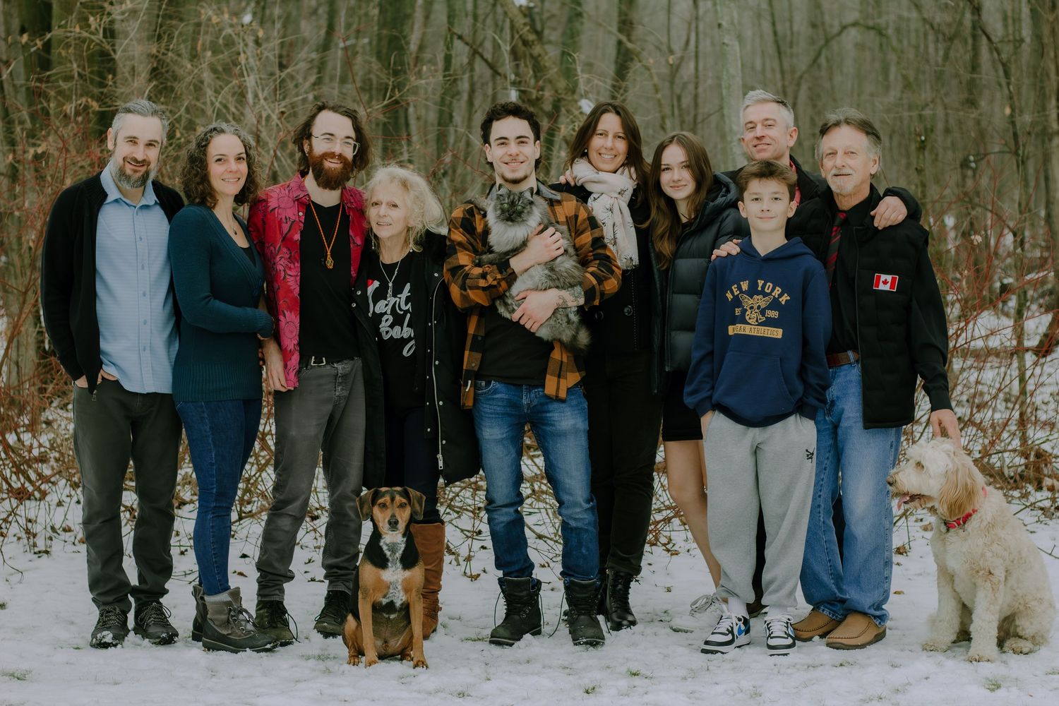 A large family group poses together in a snowy winter setting with their dogs.