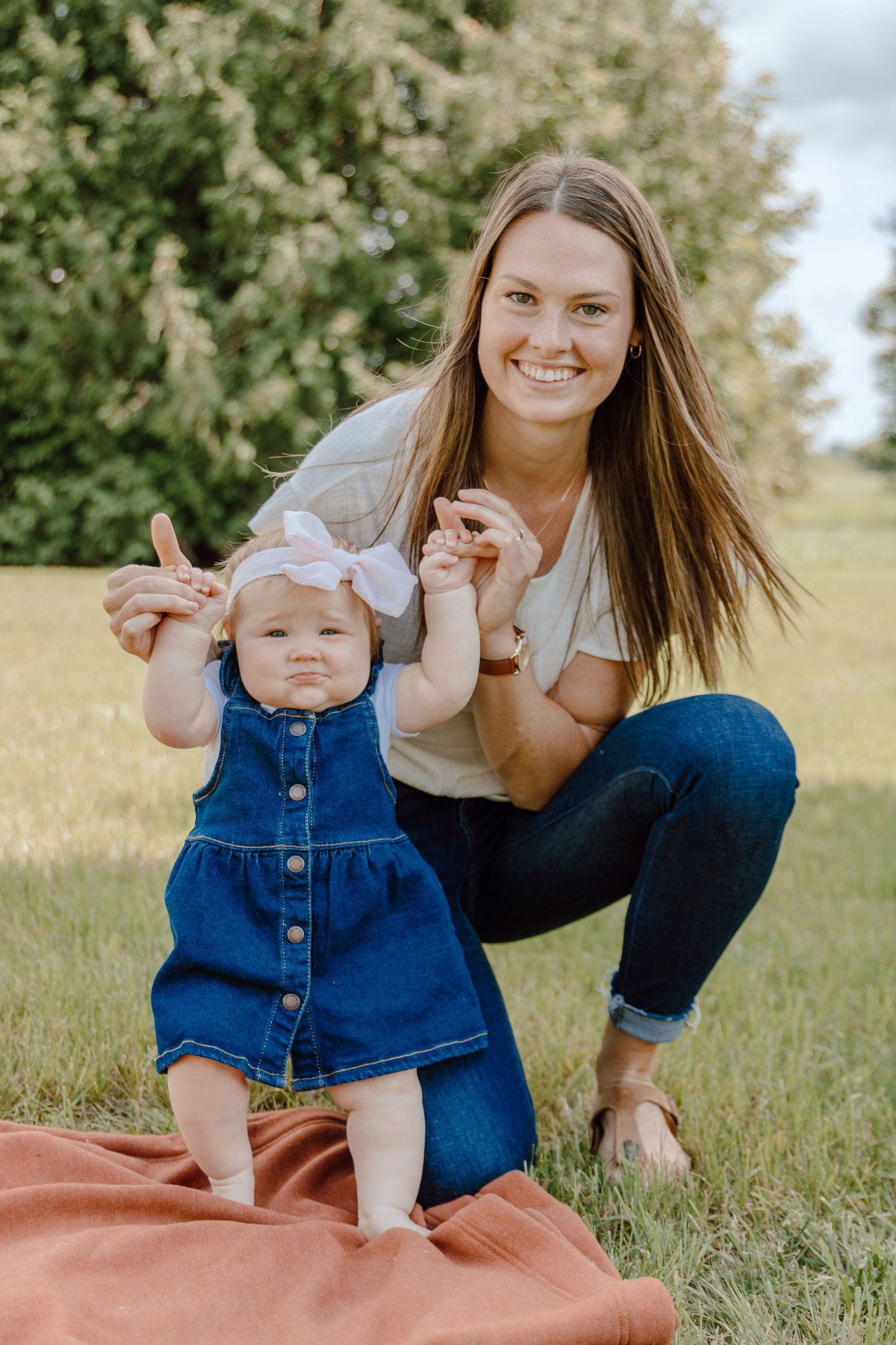 Mother and baby in denim overalls playing together on a blanket in a sunny field.