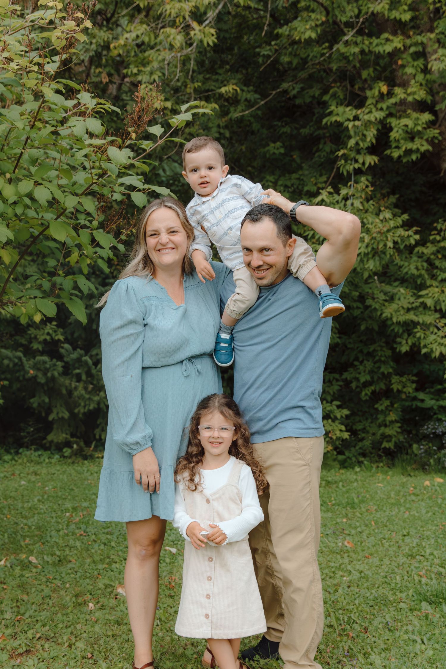 A casual outdoor family photo with parents and children arranged in a relaxed pose.