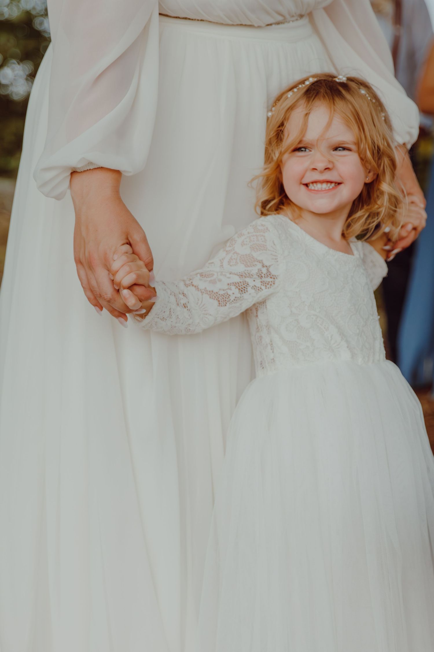 Close-up details of white lace dresses and held hands during an outdoor celebration.
