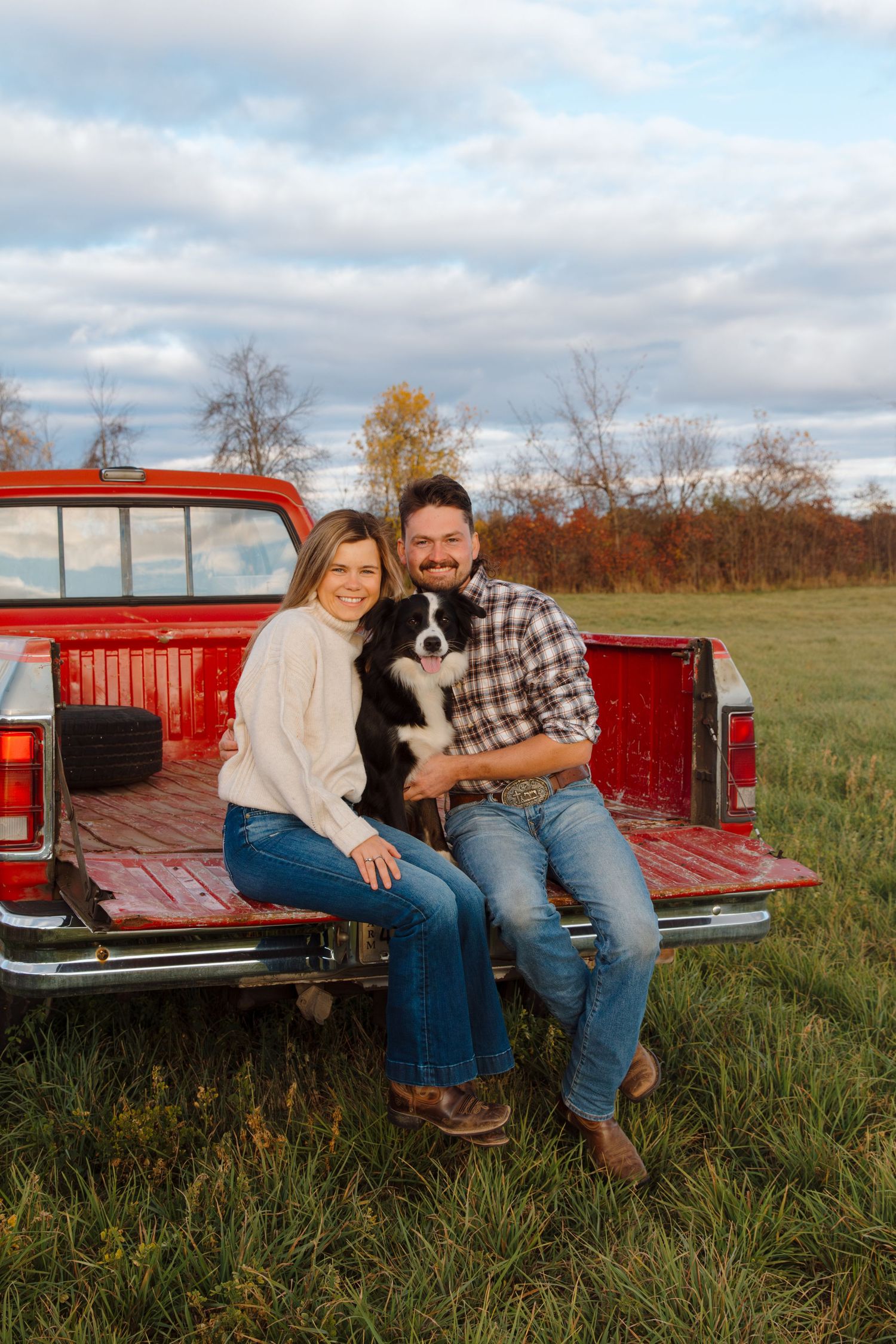 Family portrait with border collie puppy on vintage red pickup truck during golden hour.