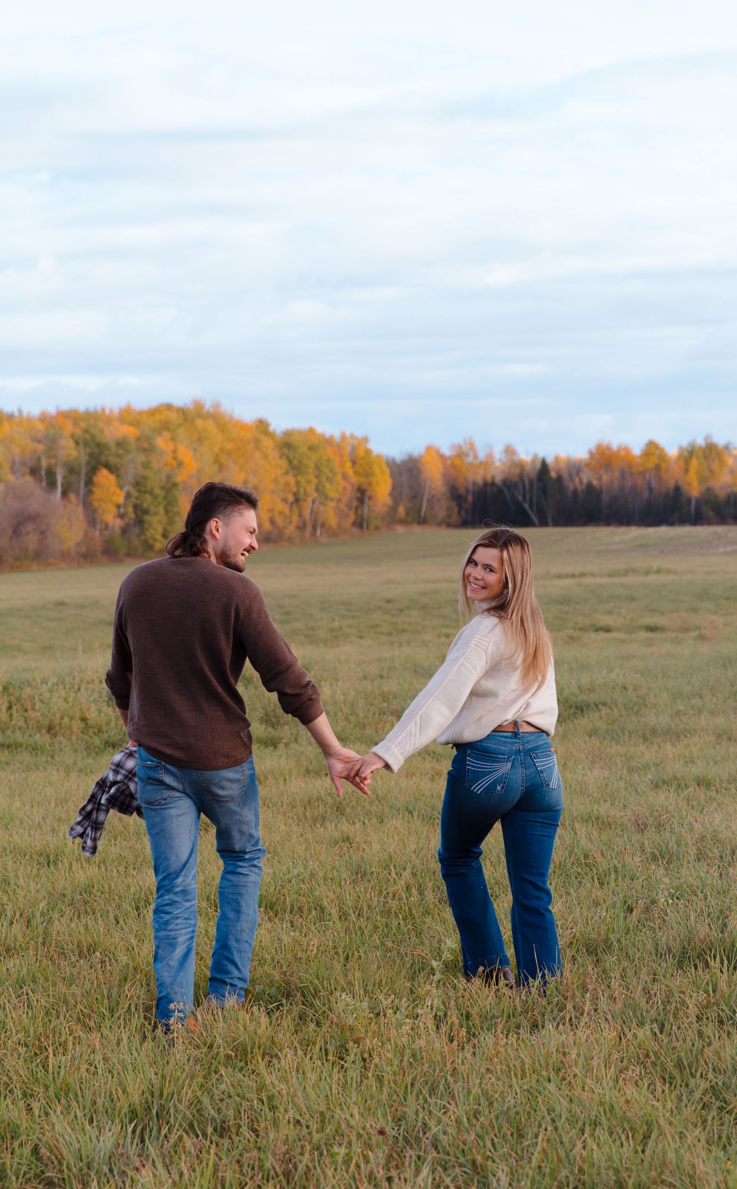 Two people playfully walk through a meadow with fall colors in the background.