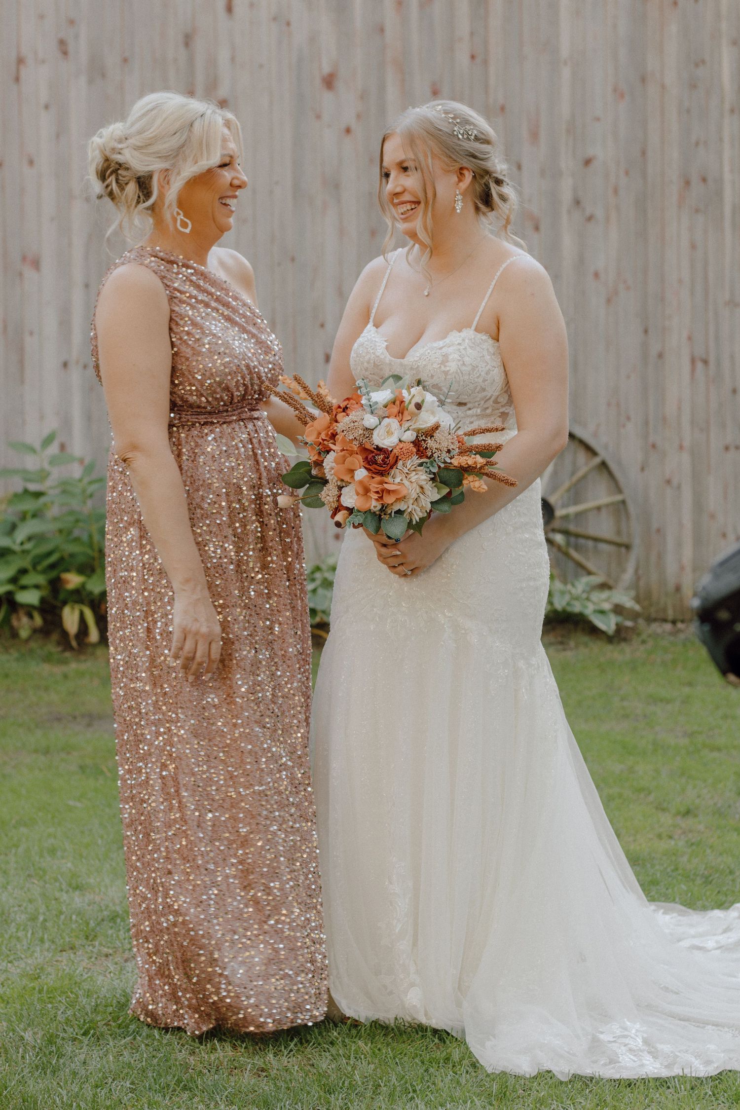 A bride in a white gown shares a moment with bridesmaid wearing a sparkly rose gold dress.