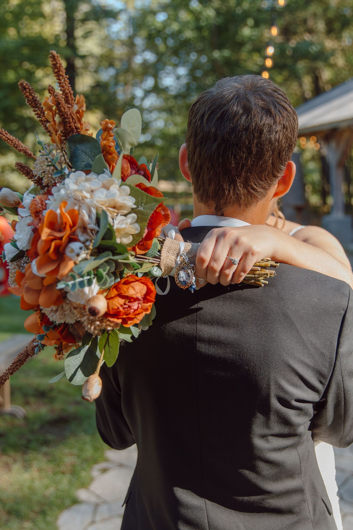 Close-up of wedding couple embracing with orange floral bouquet.
