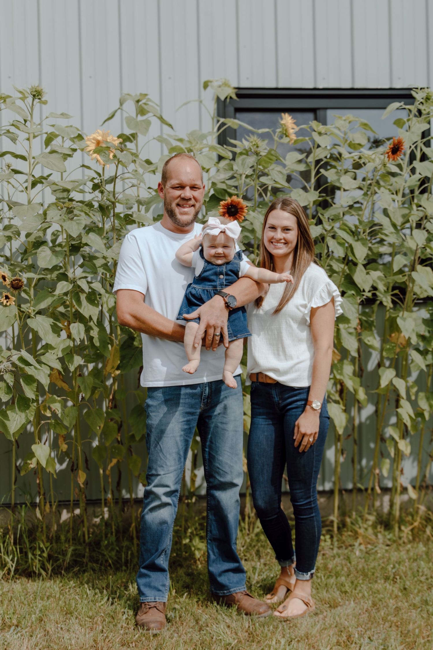 Playful family portrait session in front of tall sunflowers and grey building.