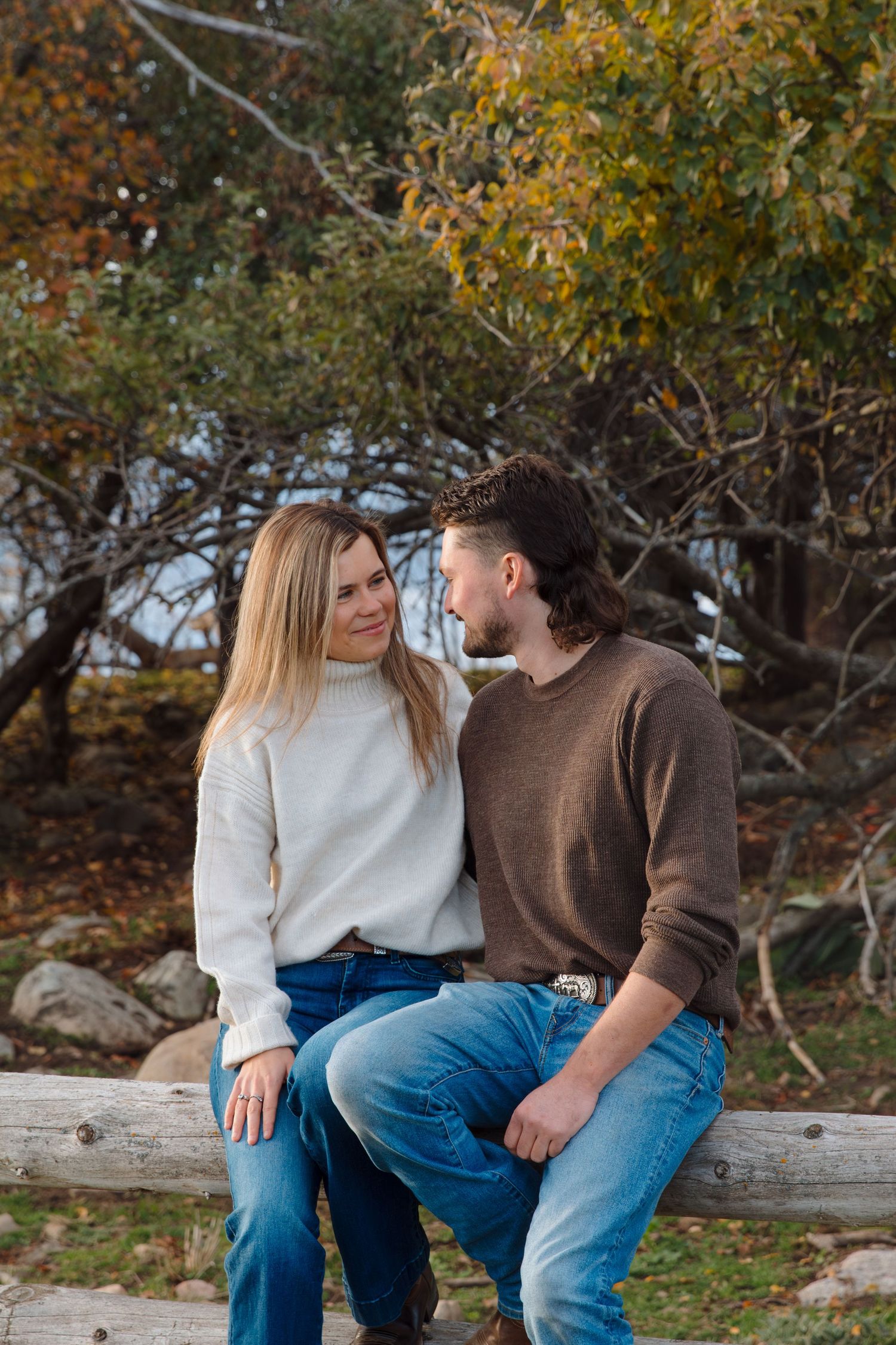 Two people share an intimate moment while sitting on a wooden fence during fall season.
