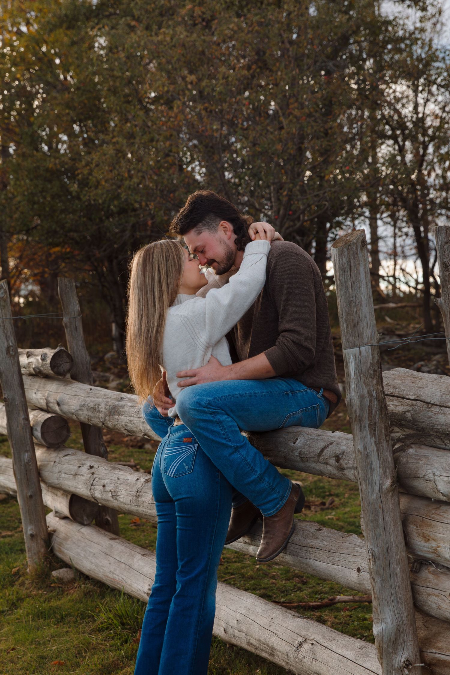 A couple shares an intimate moment against a rustic fence during golden hour.