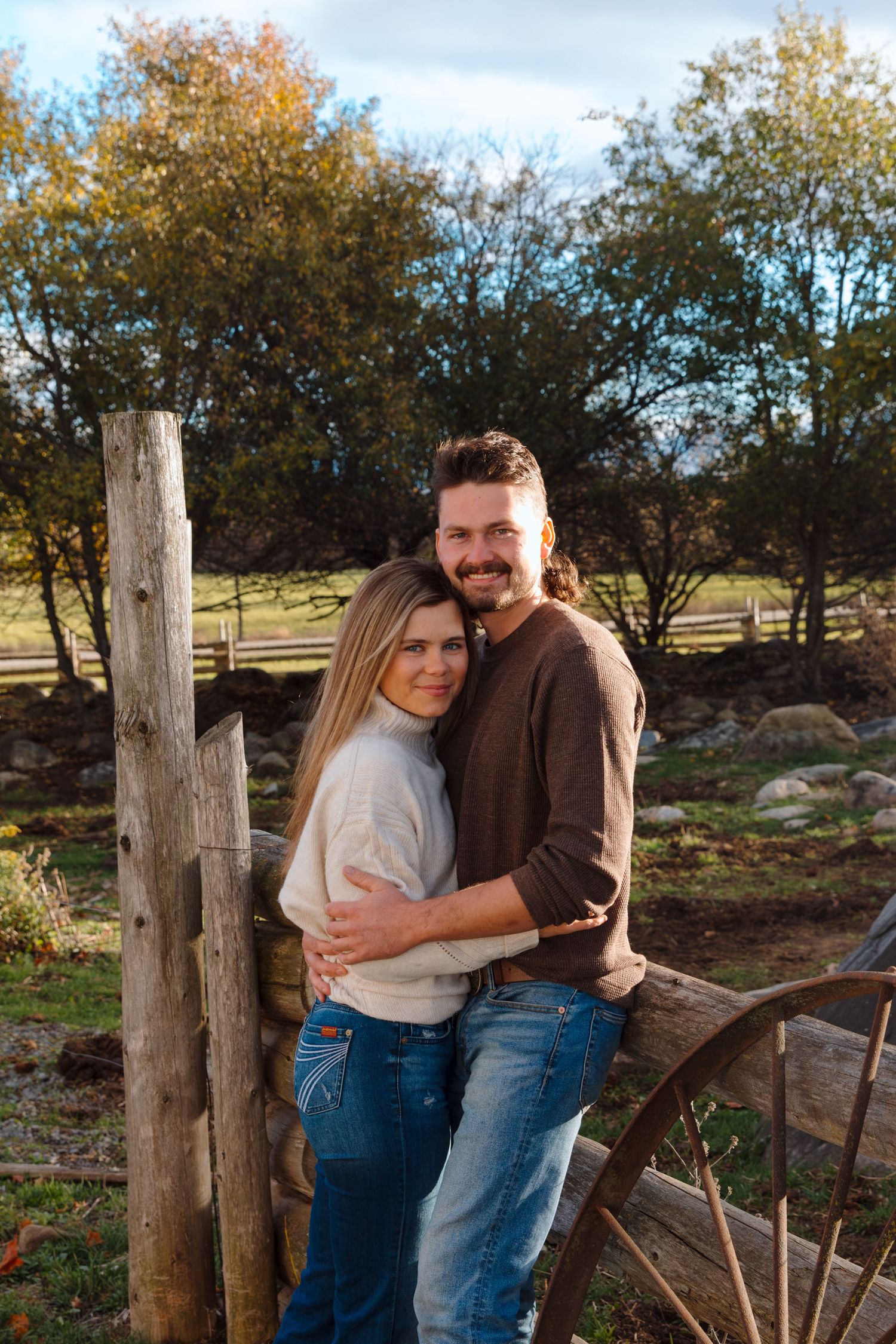 Couple in casual wear sharing intimate moment by rustic fence during fall season.