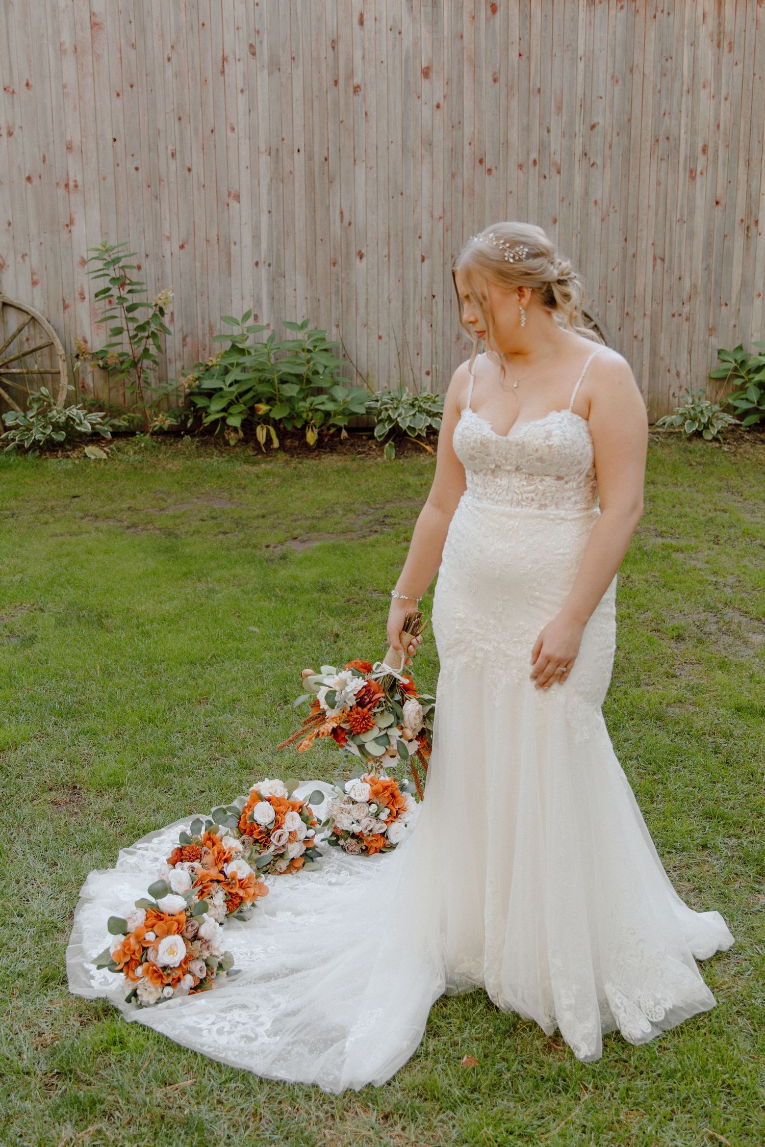 Bride in flowing white lace dress holding orange bouquet in garden setting.