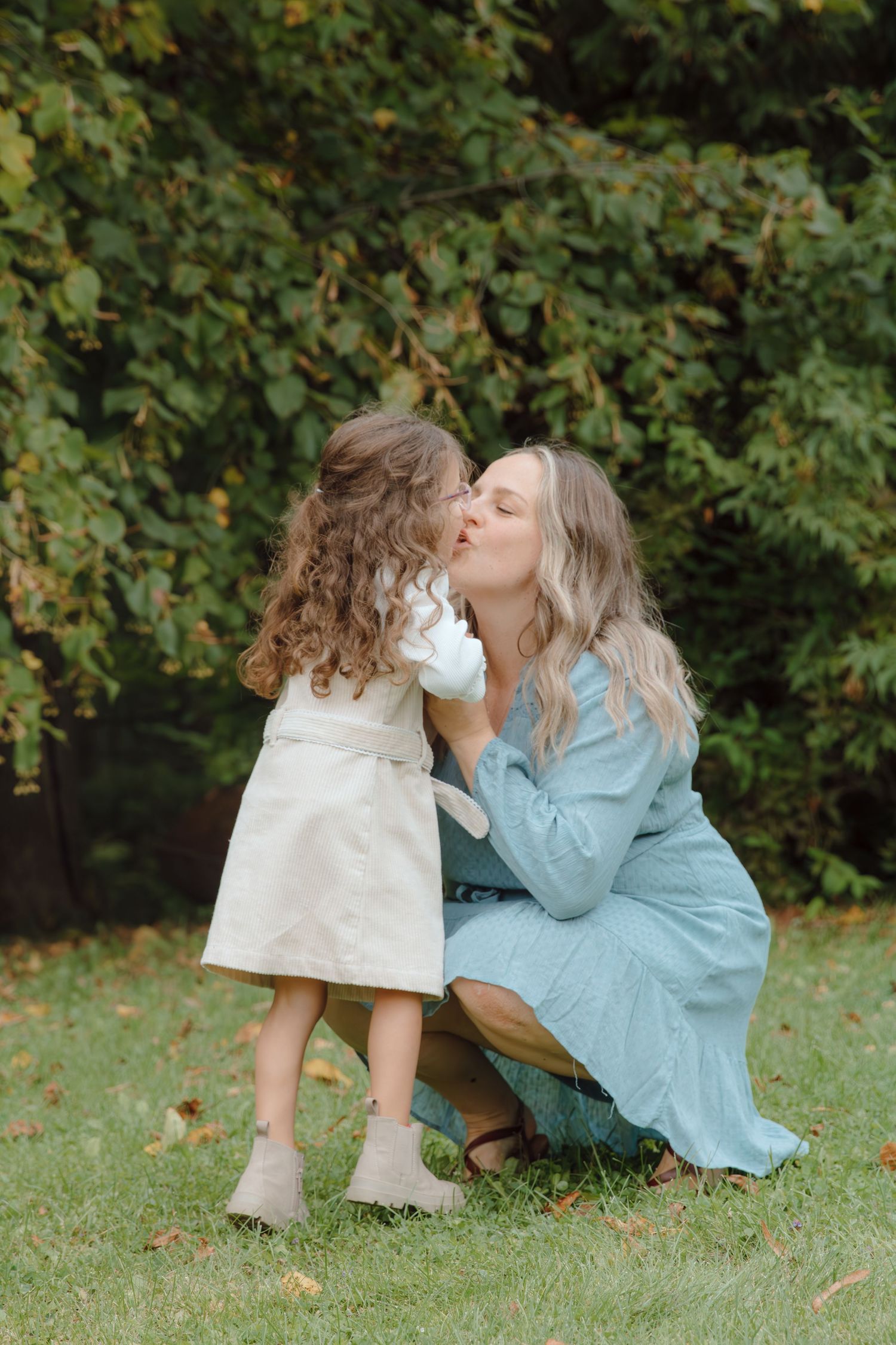 A tender moment shared between parent and child playing on grass with autumn foliage in the background.