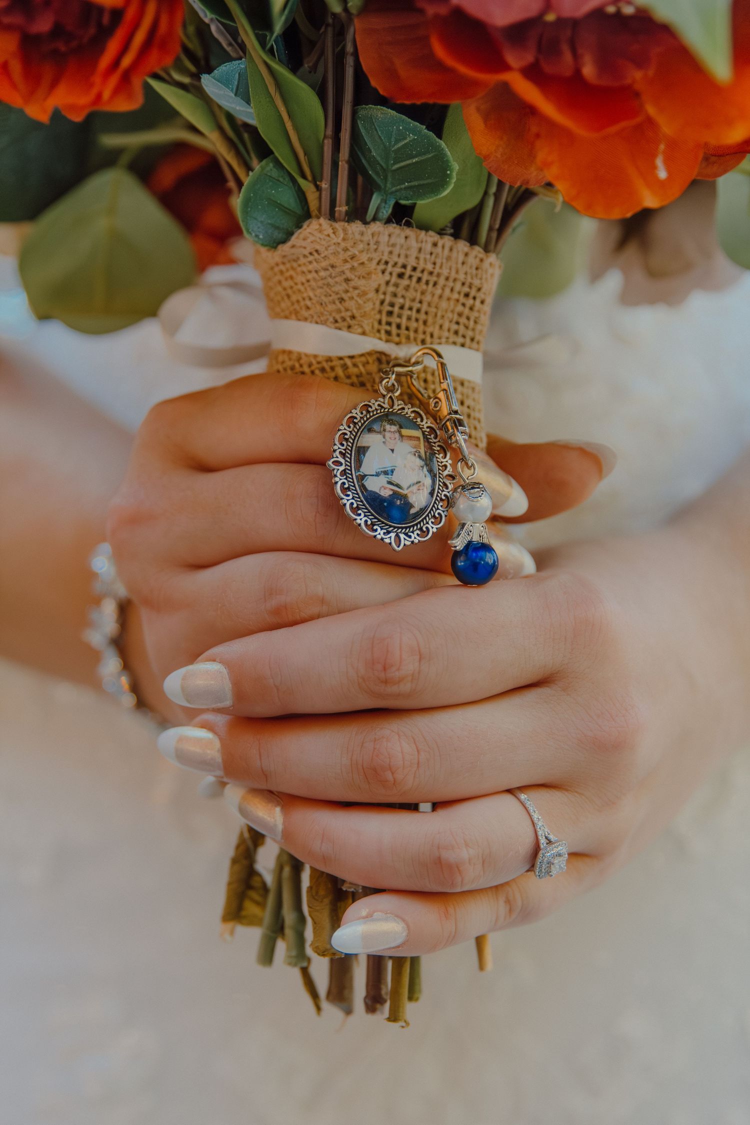 Detailed shot of hands holding orange and white wedding bouquet with vintage rings.