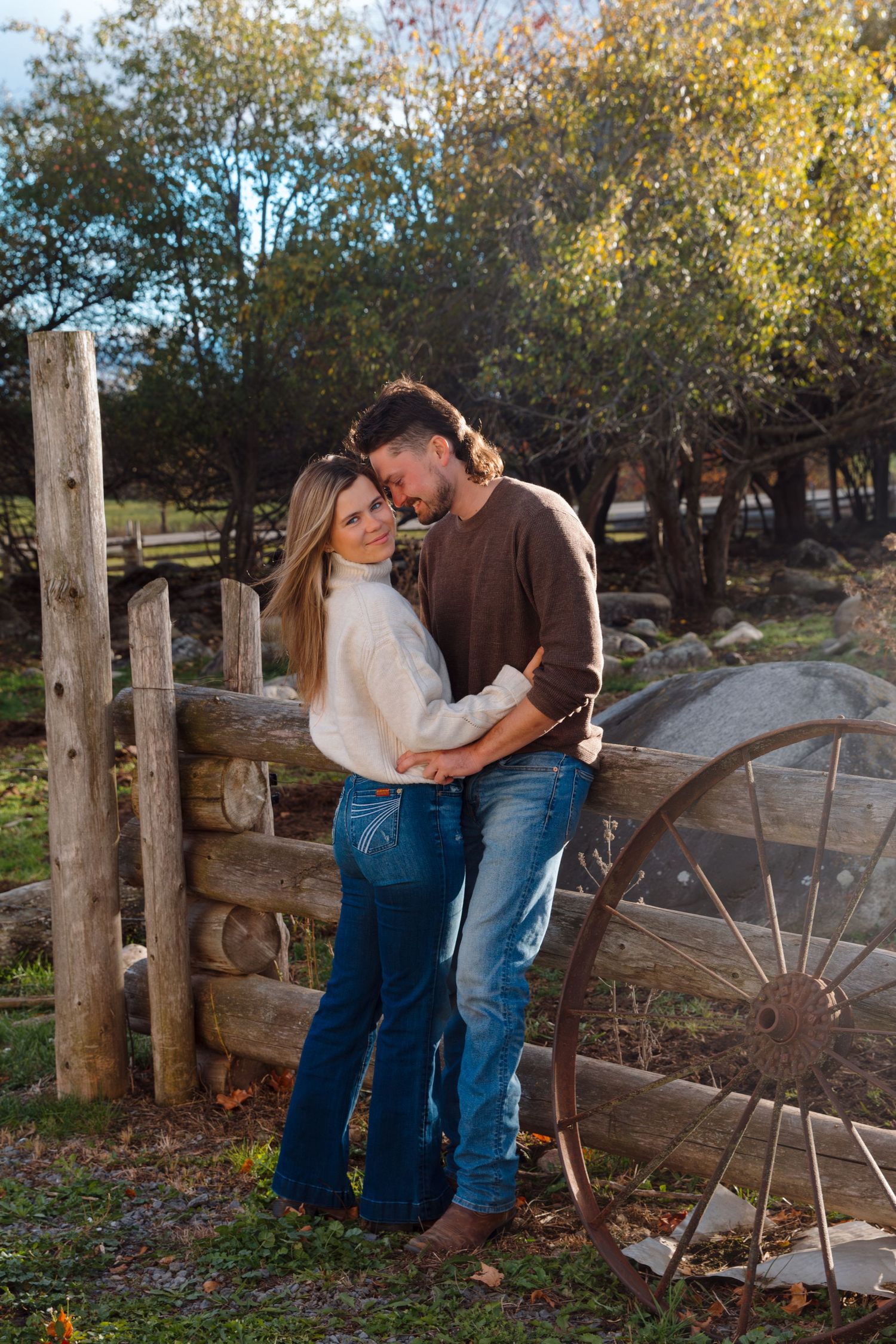 Romantic autumn photoshoot with couple by rustic fence and fallen leaves.