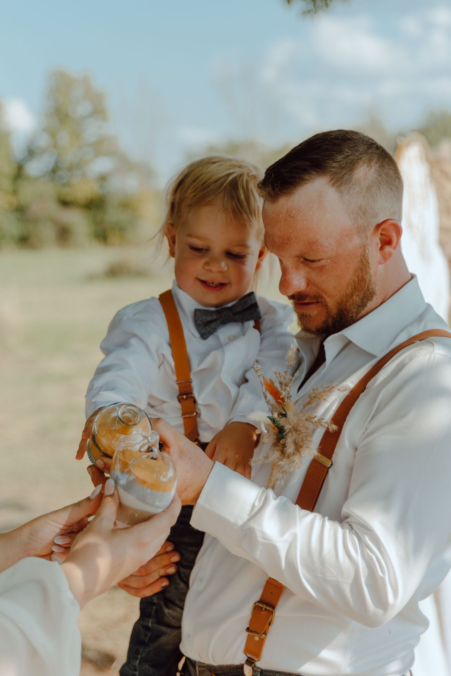 A playful moment between parent and child wearing white shirts and suspenders outdoors.
