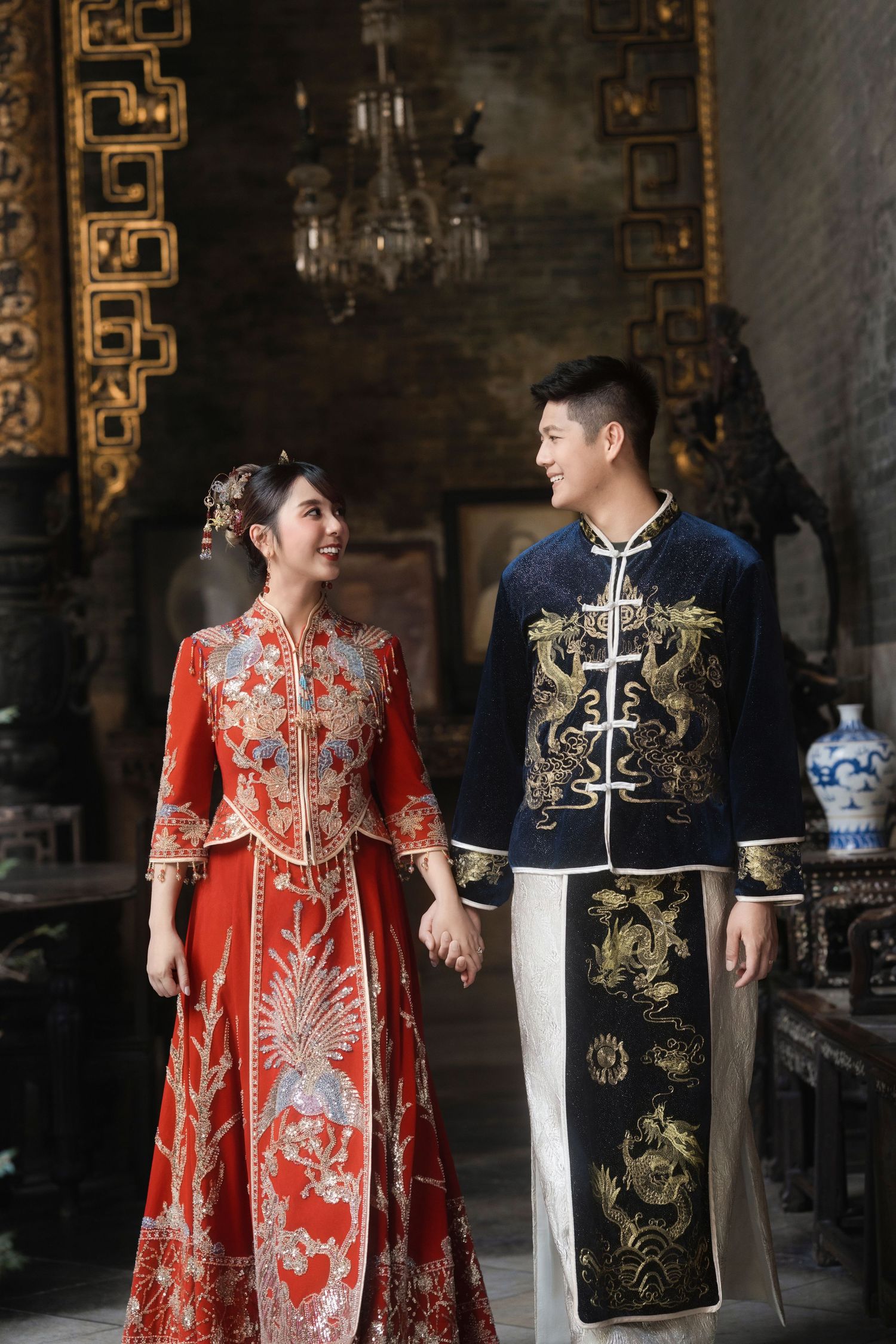 Couple walking hand-in-hand through a heritage hall while wearing traditional Chinese wedding attire at Pinang Peranakan Mansion