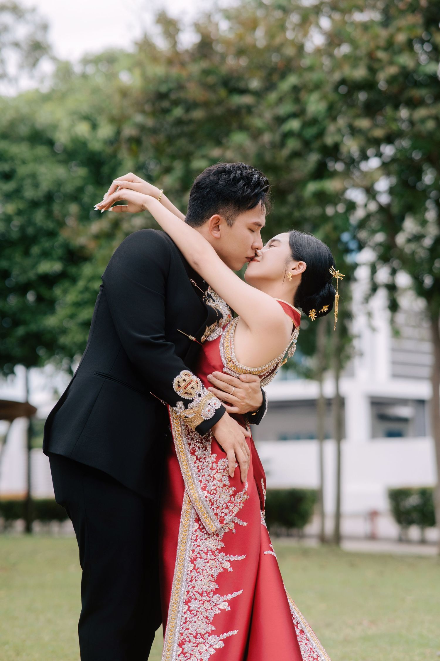 Romantic kiss during a traditional Chinese wedding with the couple wearing modern red and black embroidered silk outfits