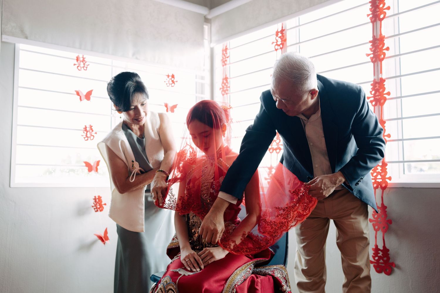 A bride being veiled by her parents in a room decorated for a traditional Chinese wedding