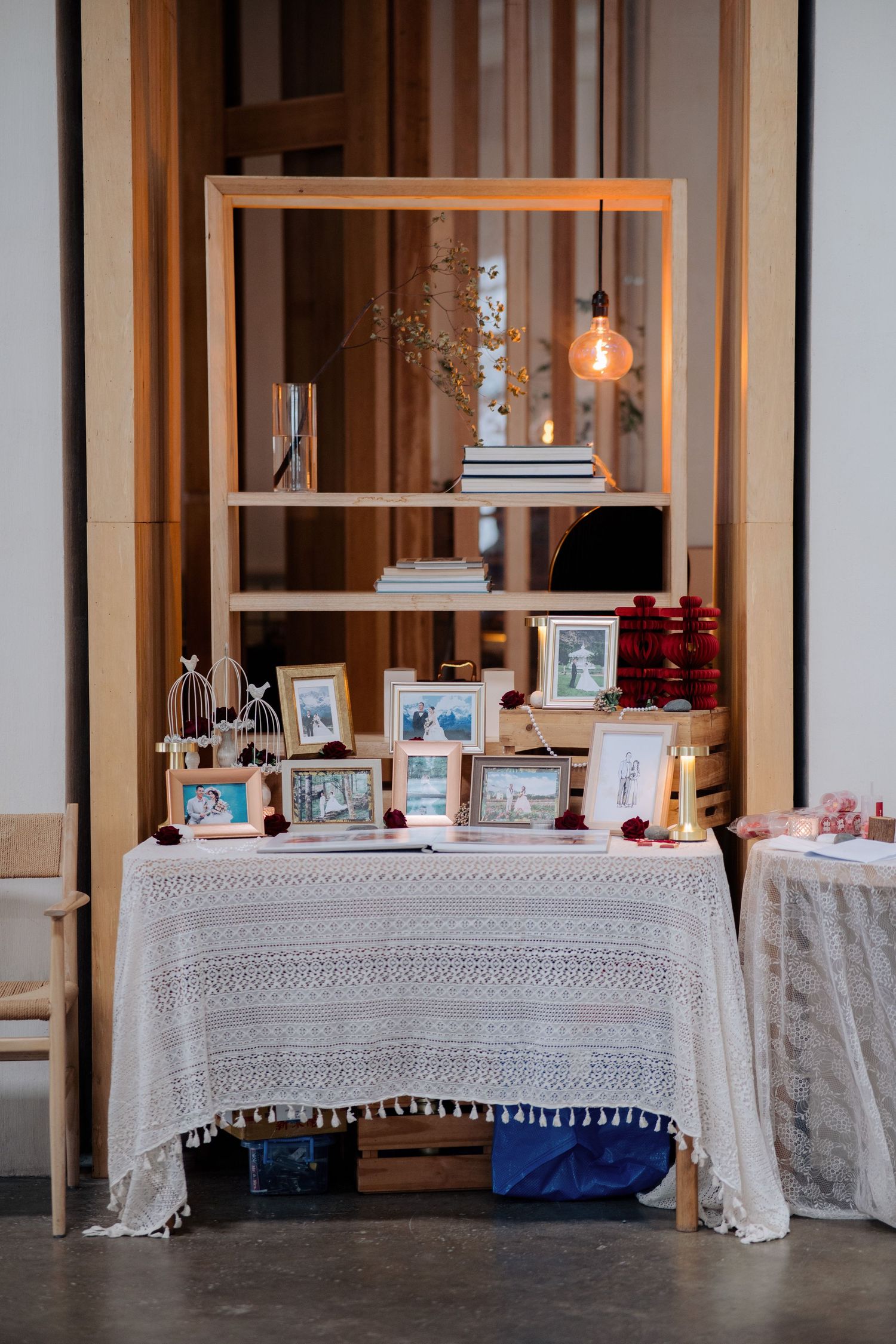 Wedding welcome table with a lace tablecloth, framed photos, and a warm hanging light bulb in a wooden frame